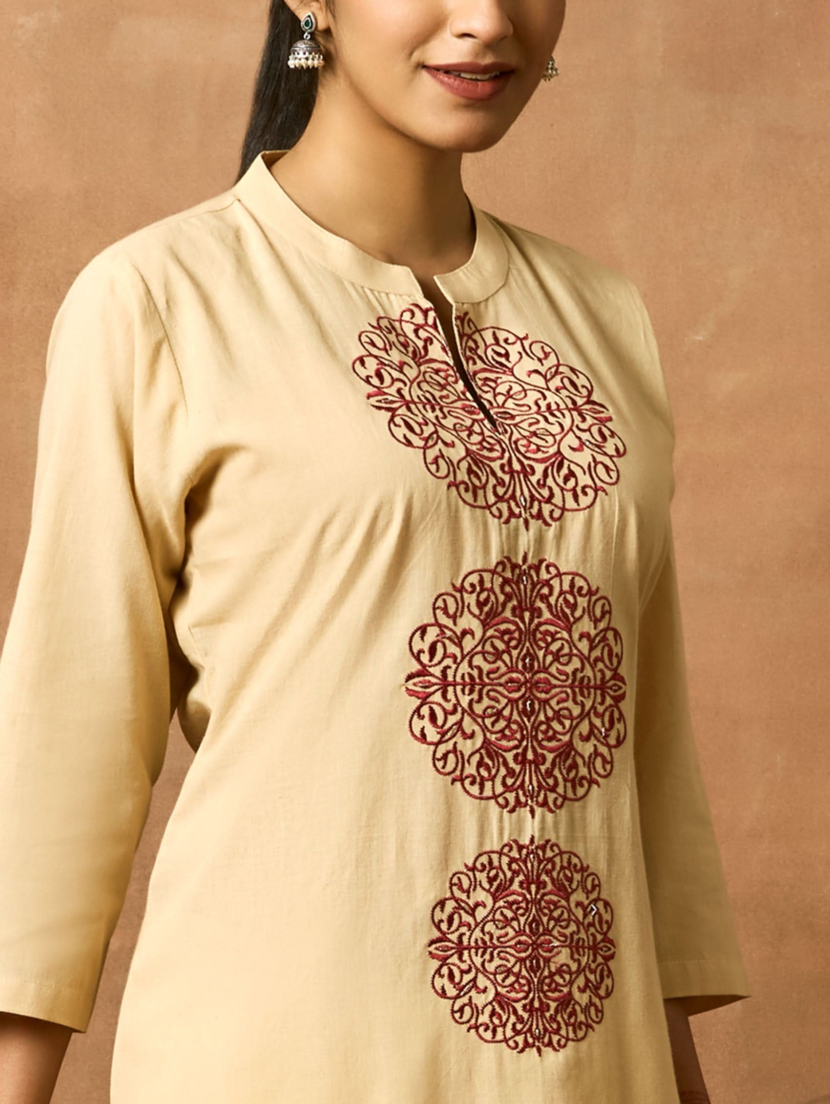 A woman plus-size model wearing a beige kurta with ban collar and three-fourth sleeves, featuring computerised thread embroidery.