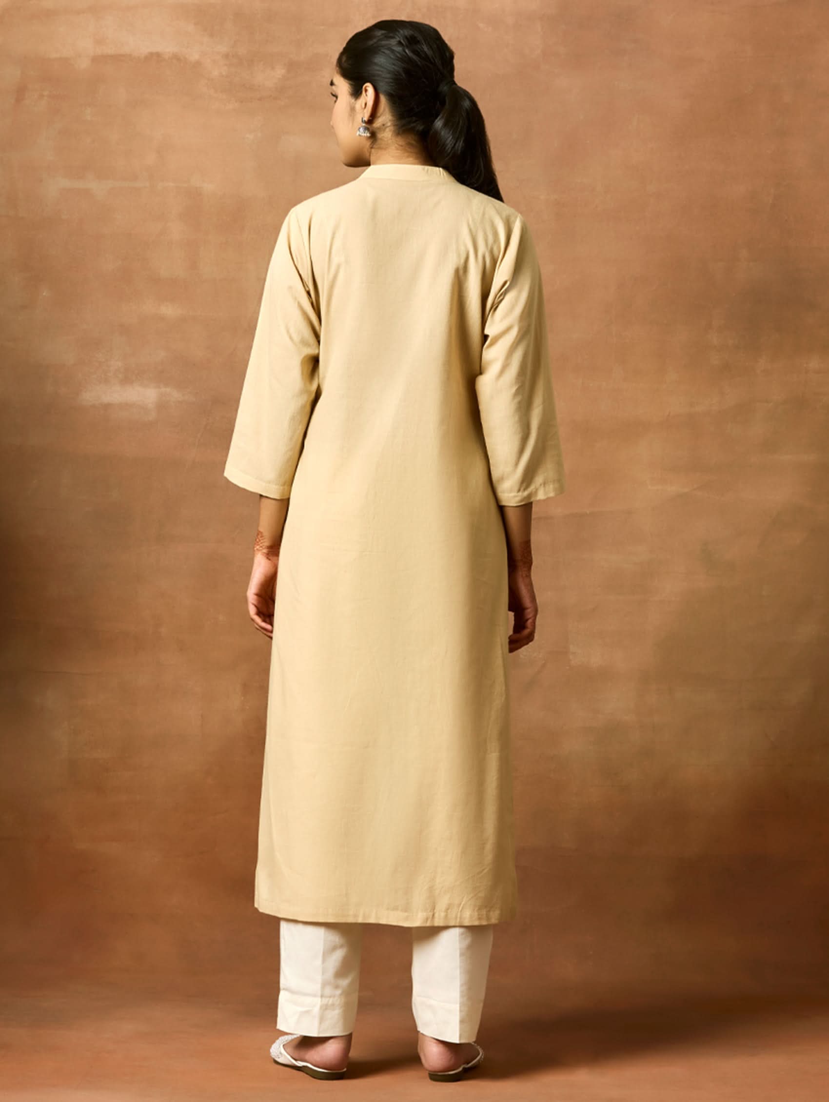 A woman plus-size model wearing a beige kurta with ban collar and three-fourth sleeves, featuring computerised thread embroidery.