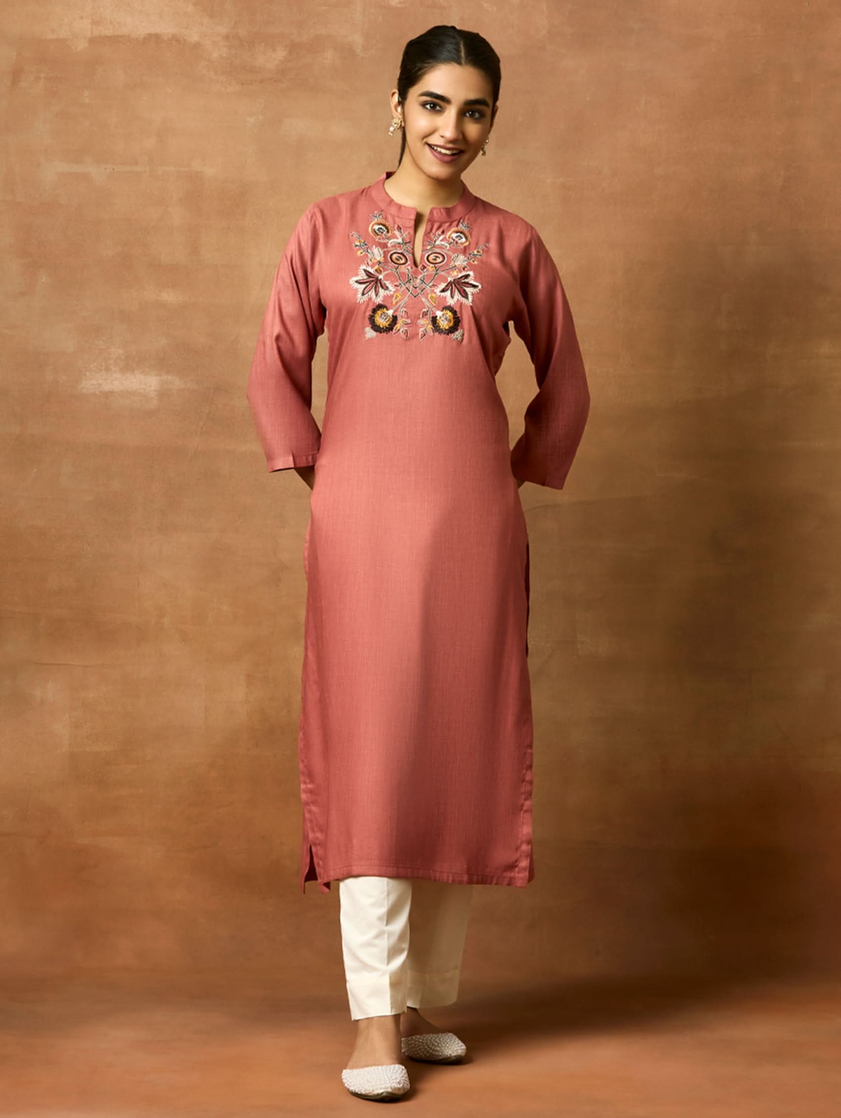 A woman plus-size model wearing a pink rayon slub kurta with ban collar, three-fourth sleeves, and side slits. The kurta has computerised thread embroidery on the front.