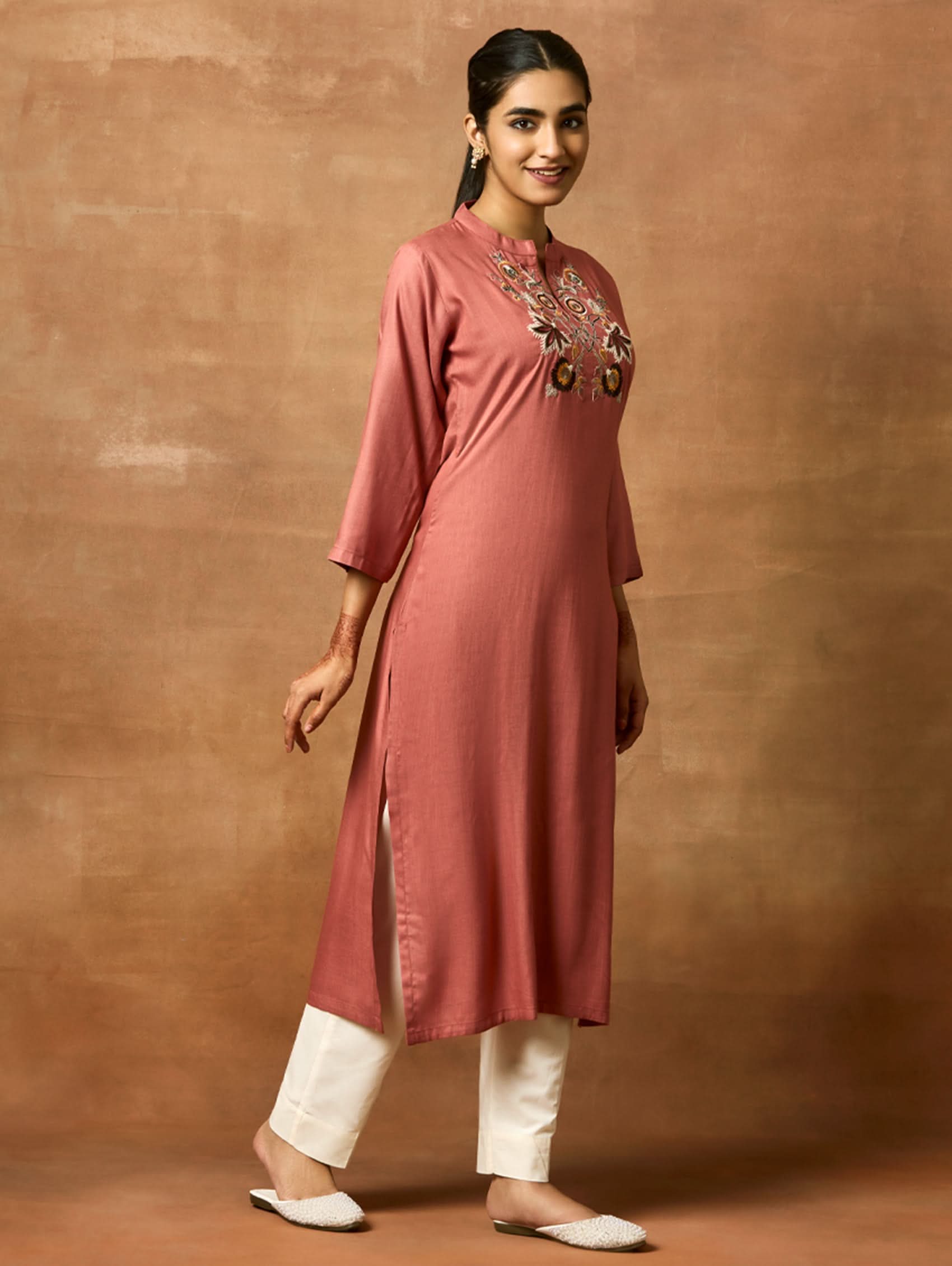 Woman wearing a rust-colored kurta with embroidery on a brown background.