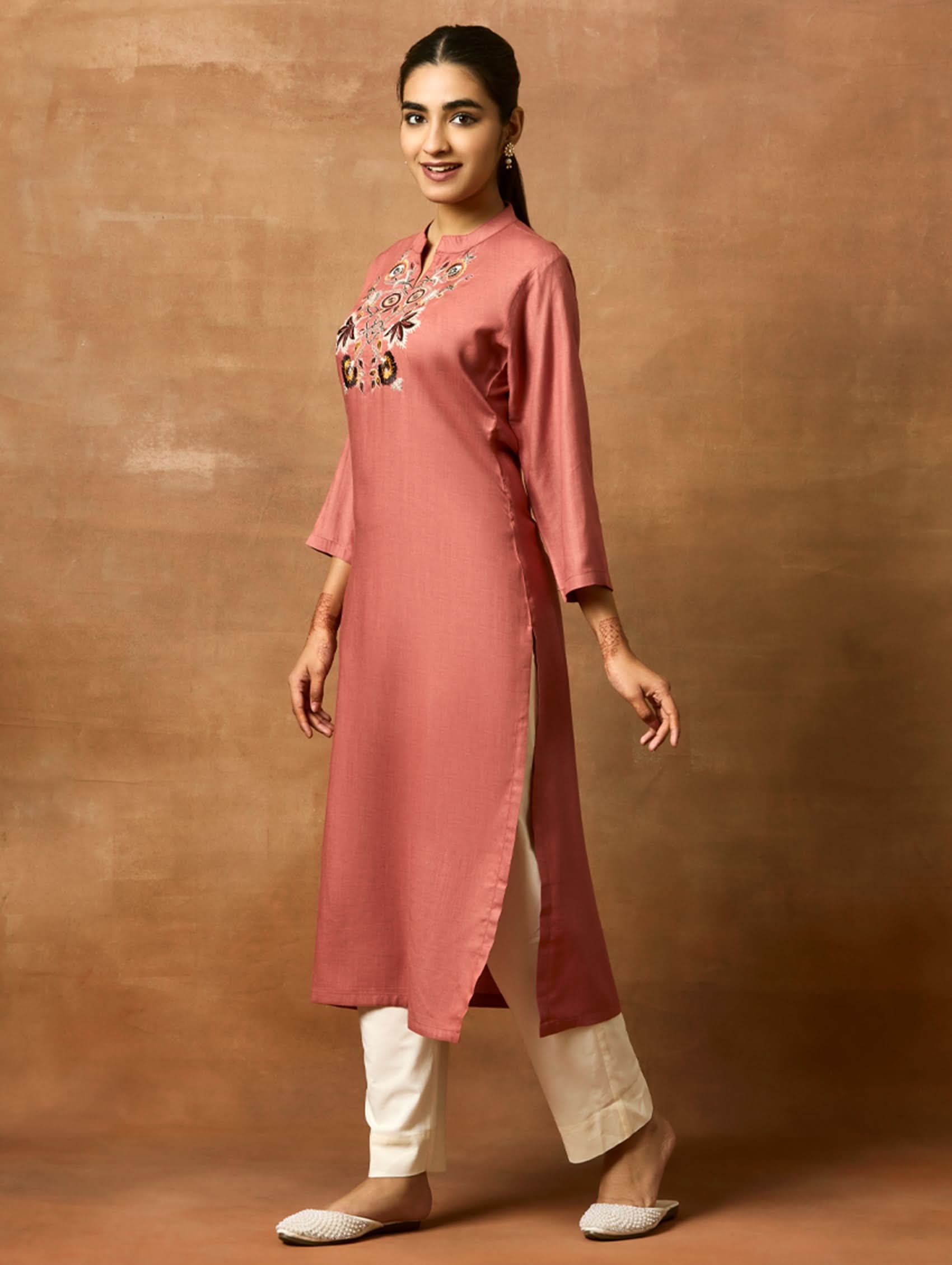 Woman wearing a pink kurta with embroidery on a brown background