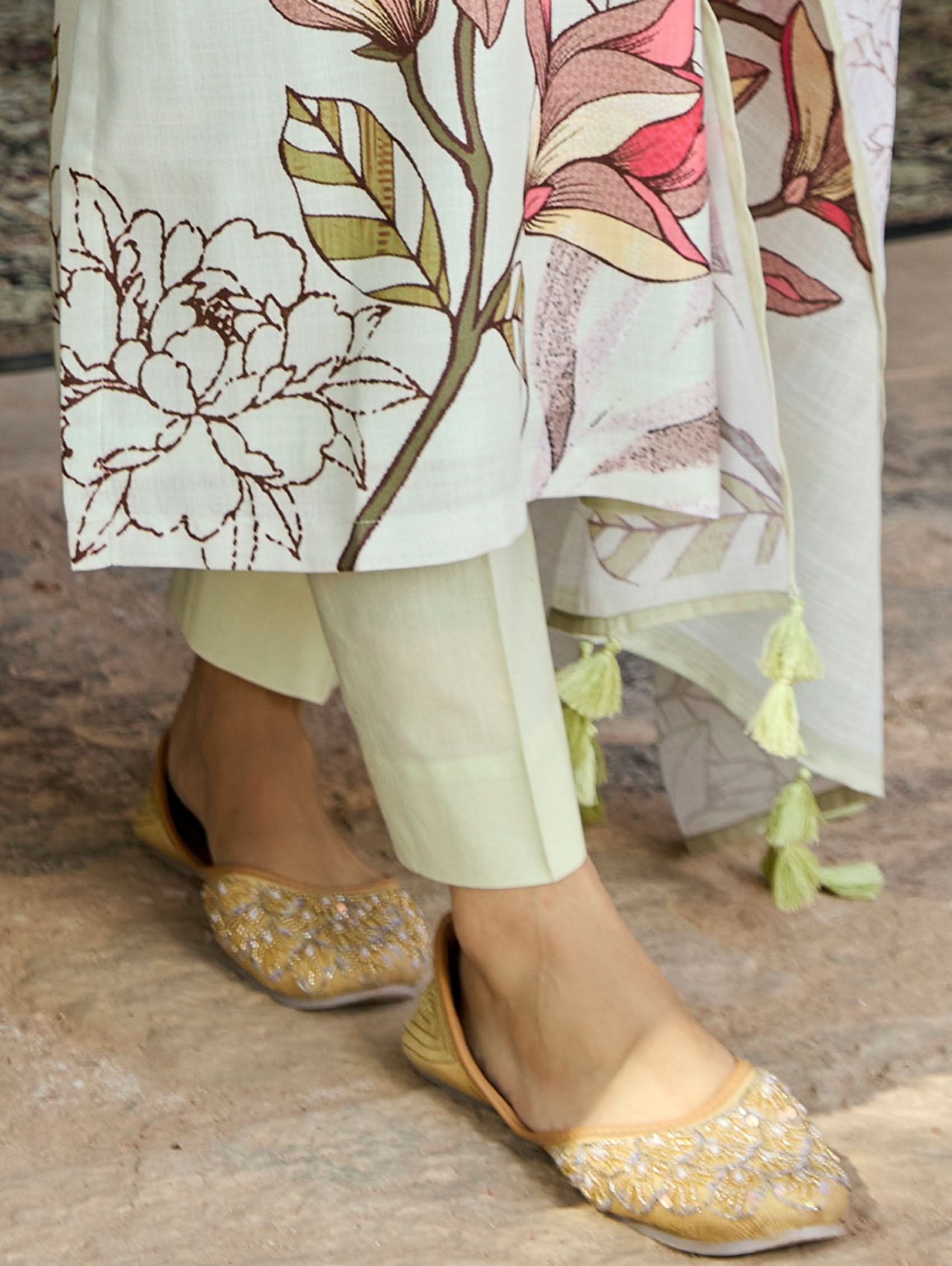 A woman standing in an archway, wearing a digitally printed cotton linen suit set with a round neckline kurta, three-fourth sleeves, side slits, and a dupatta with a floral pattern.