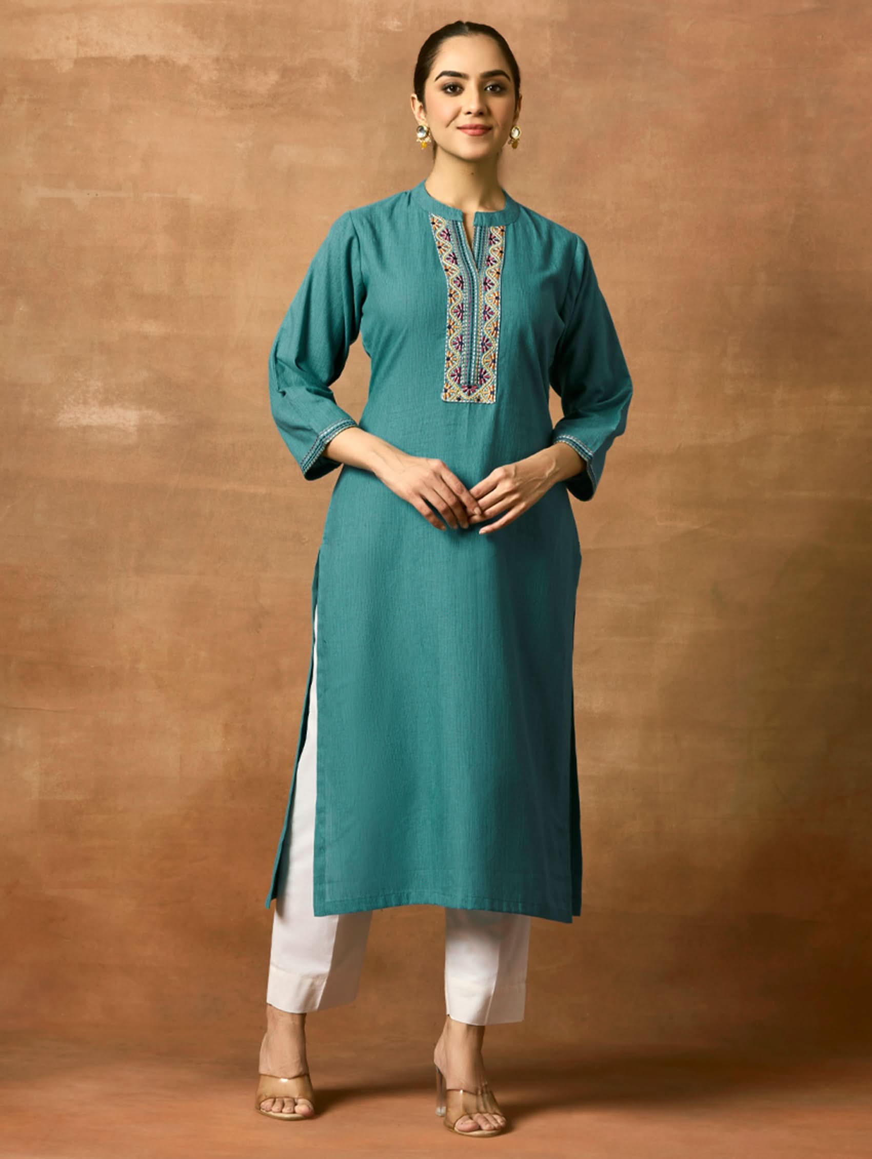 A woman plus-size model wearing a green pure cotton kurta with a ban collar, three-fourth sleeves, and side slits. The kurta has computerised thread embroidery on it.