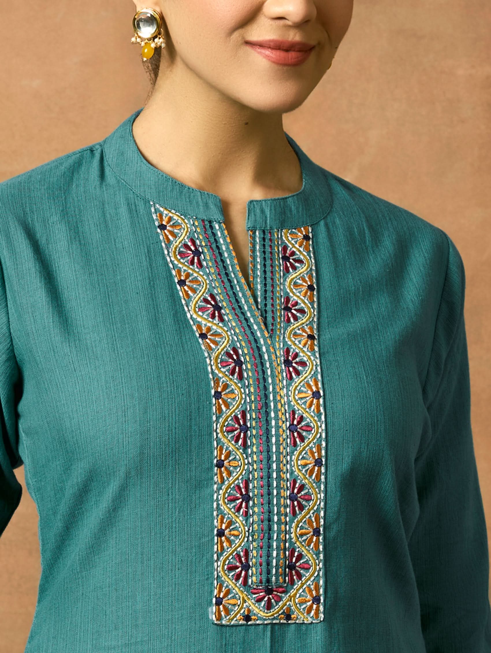 Close-up of a teal garment with intricate embroidery against a plain background.