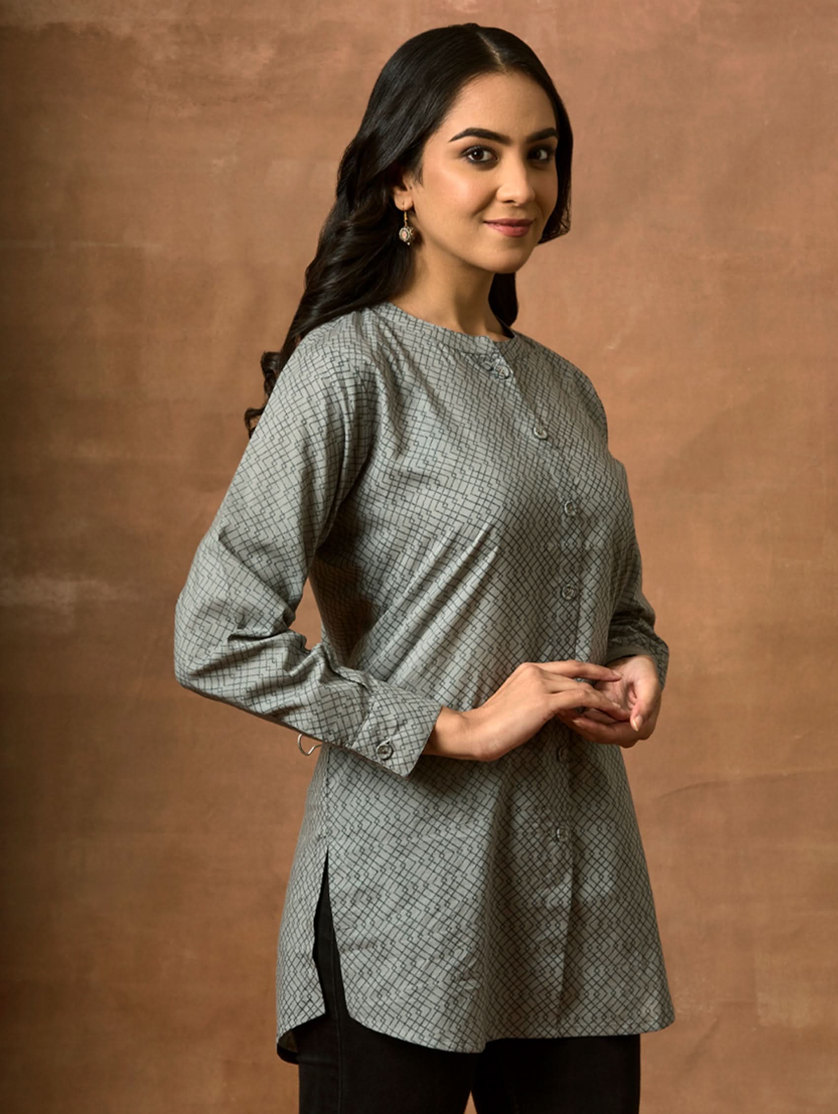 A woman wearing a gray and white printed pure cotton short kurti with a mandarin collar, full sleeves, and side slits.