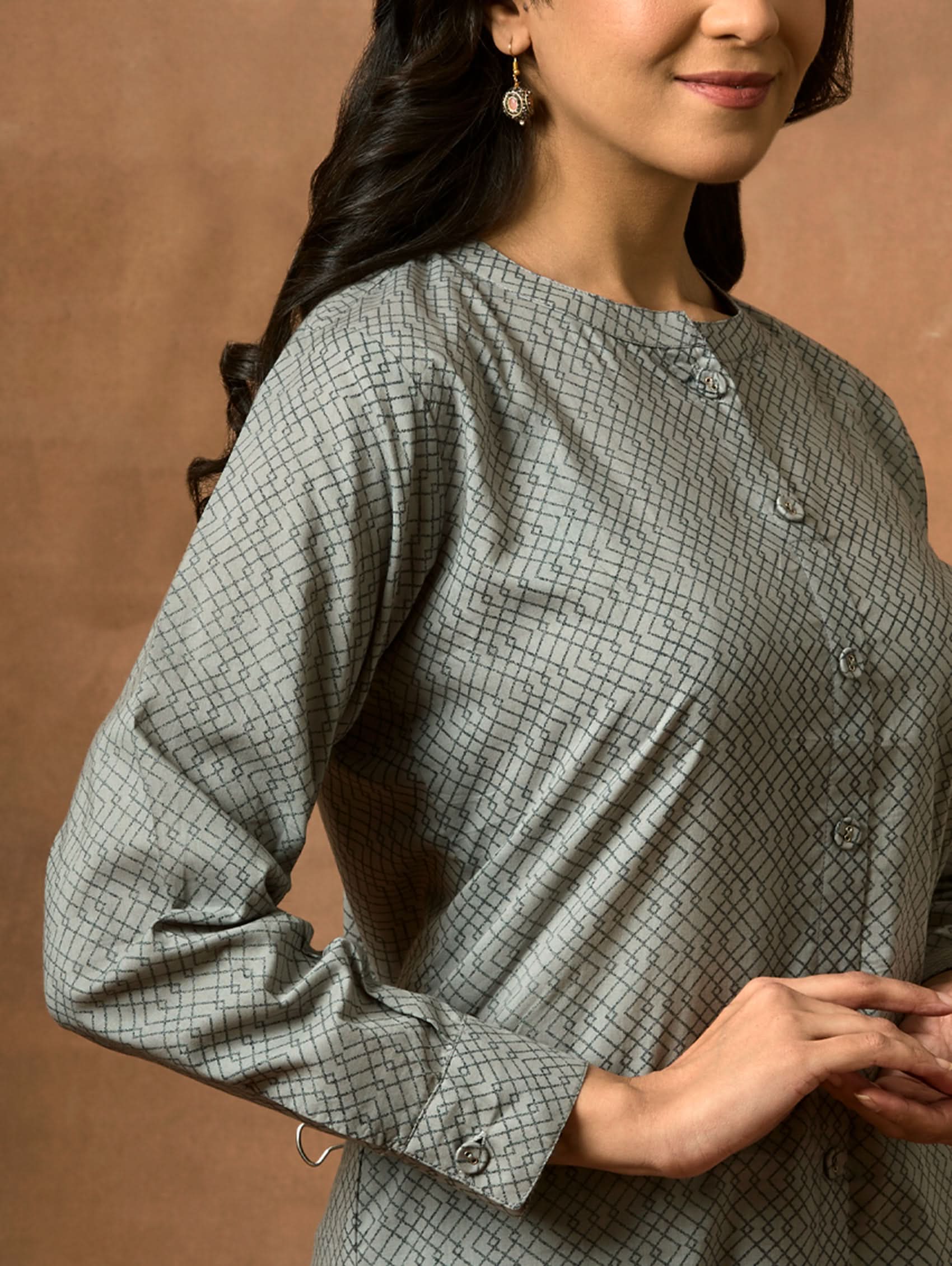 A woman wearing a gray and white printed pure cotton short kurti with a mandarin collar, full sleeves, and side slits.