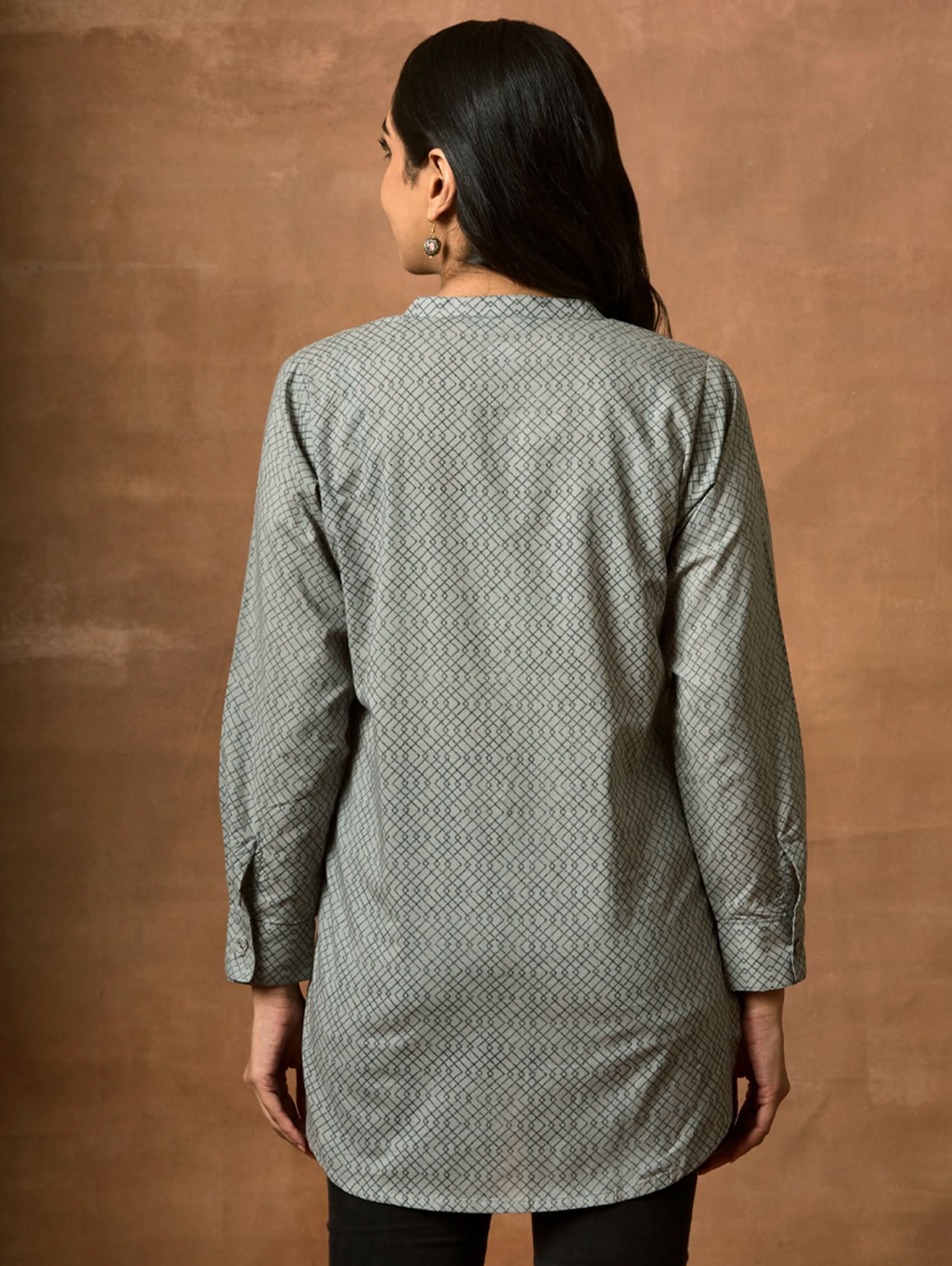 A woman wearing a gray and white printed pure cotton short kurti with a mandarin collar, full sleeves, and side slits.