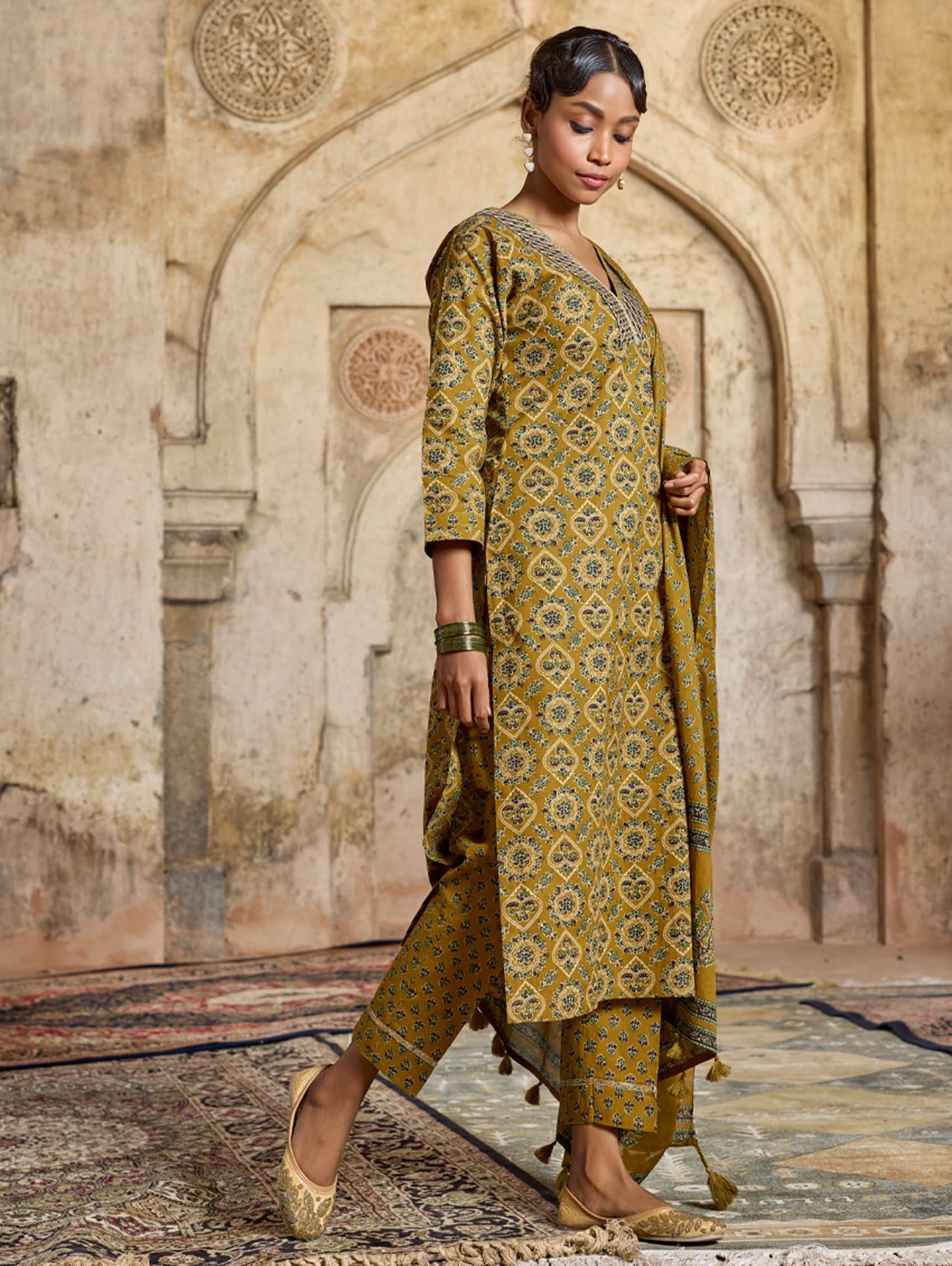 A model wearing a yellow and green embroidered pure cotton suit set with a kurta, pants, and a dupatta.