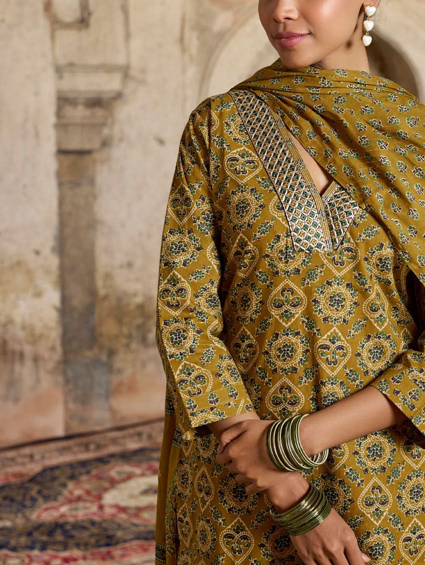 A model wearing a yellow and green embroidered pure cotton suit set with a kurta, pants, and a dupatta.