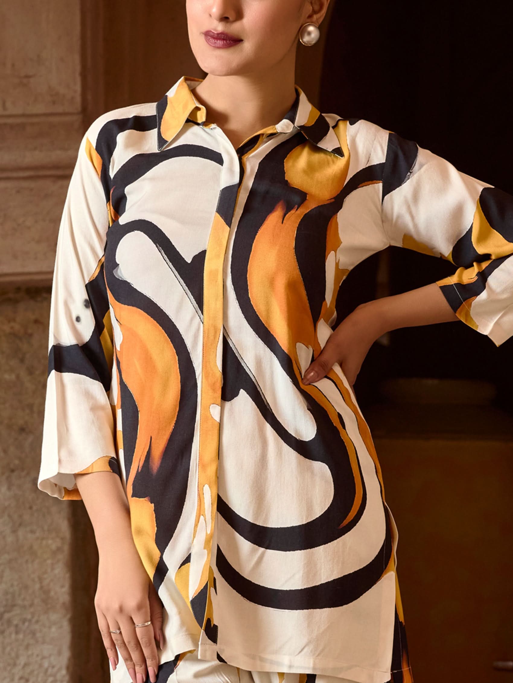 A model wearing a short kurta with a revere collar and three-fourth sleeves, paired with pants that have partially elasticated waistband and pockets on either side. The fabric is digitally printed viscose rayon.