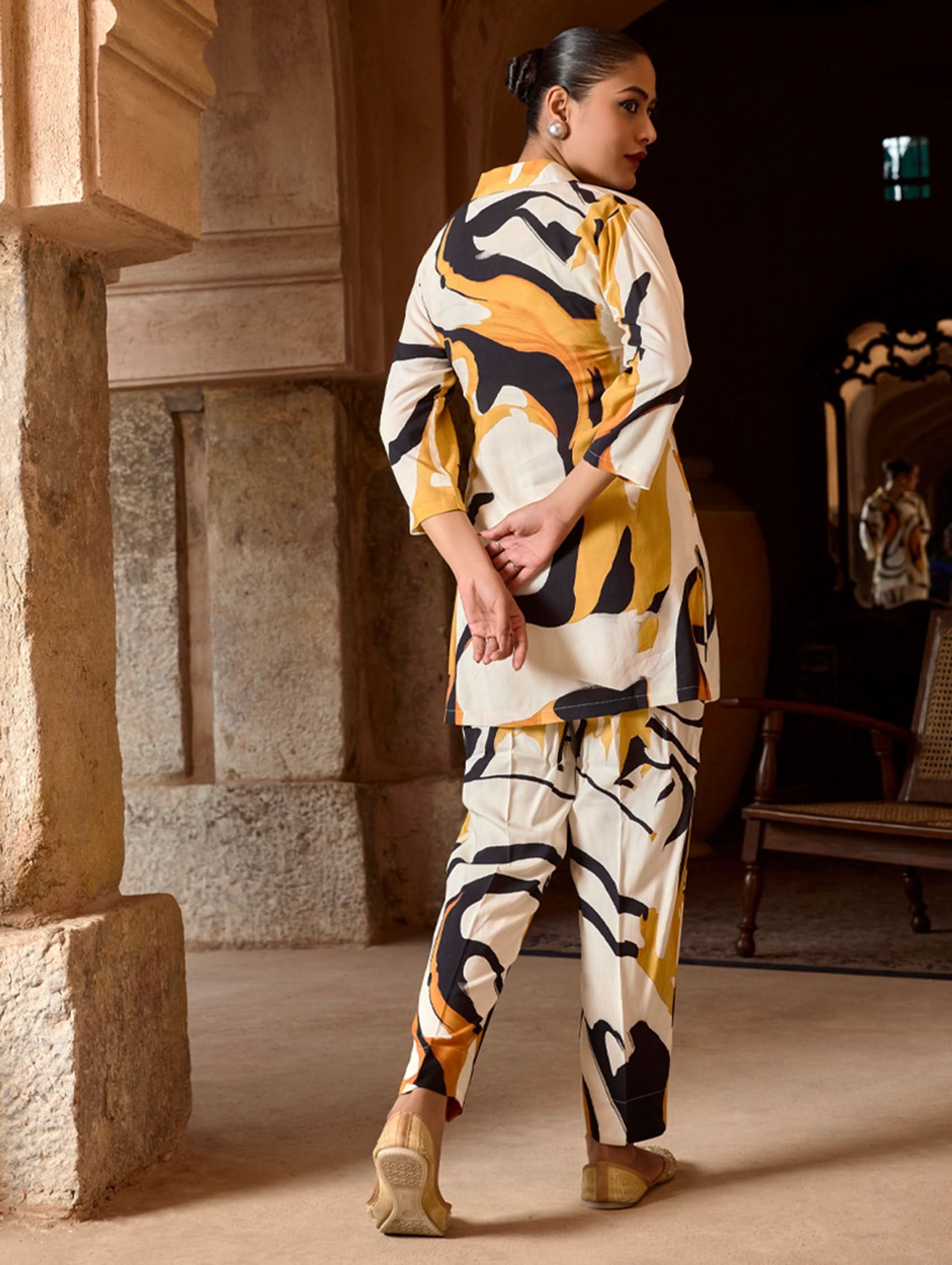 A model wearing a short kurta with a revere collar and three-fourth sleeves, paired with pants that have partially elasticated waistband and pockets on either side. The fabric is digitally printed viscose rayon.