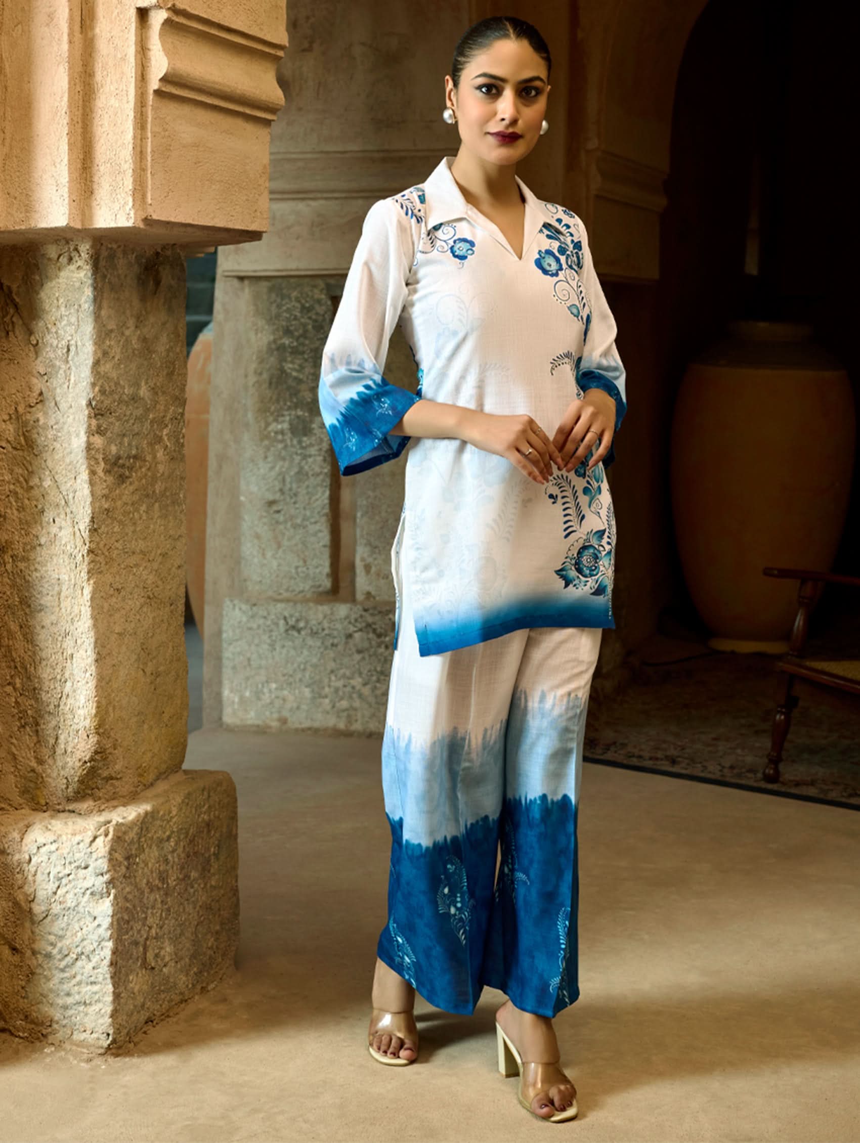 A woman wearing a digitally printed cotton linen short kurta with a revere collar and three-quarter sleeves, paired with straight pants. The outfit features blue and white colors with hand embroidery on the kurta.