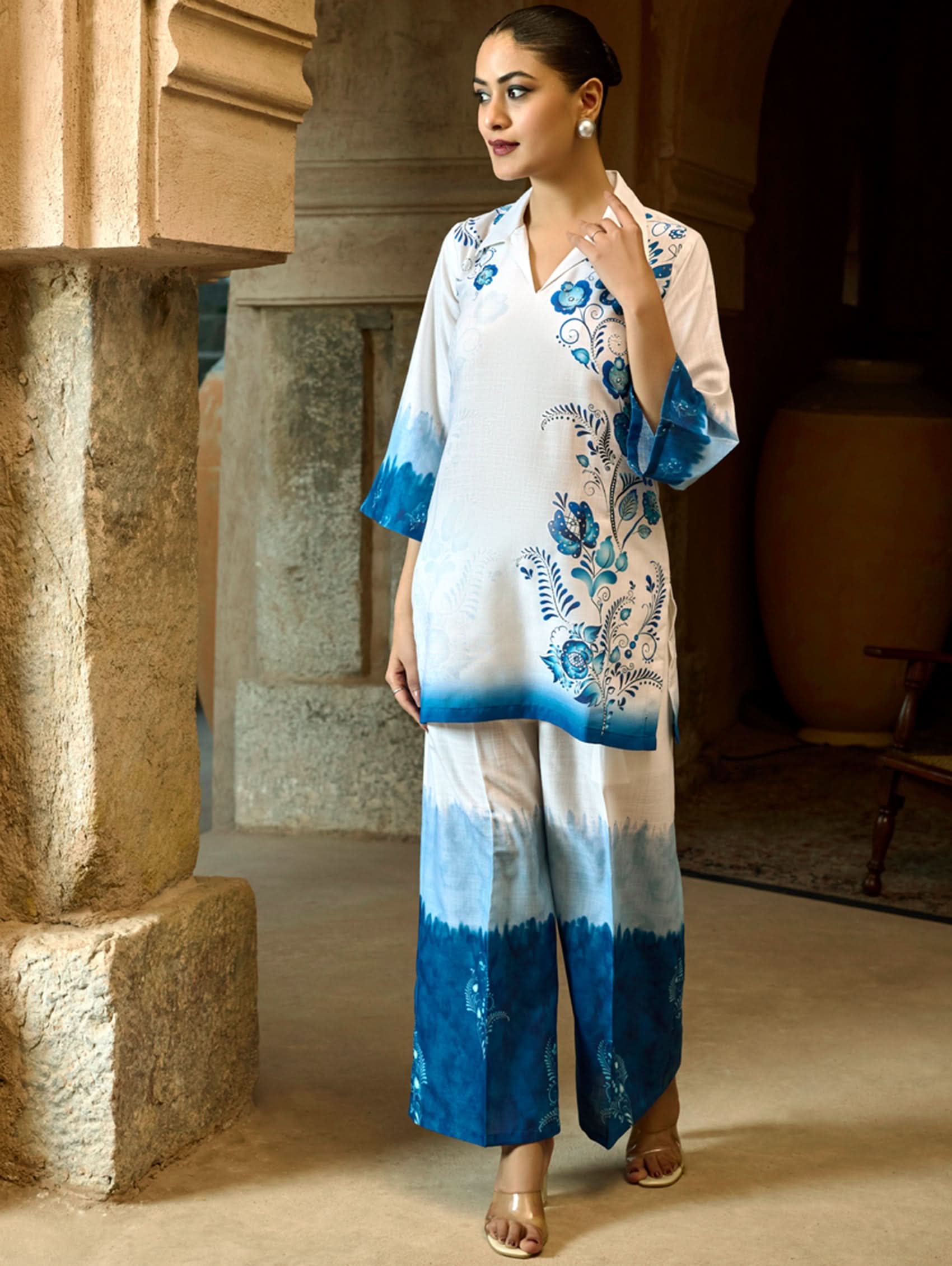 A woman wearing a digitally printed cotton linen short kurta with a revere collar and three-quarter sleeves, paired with straight pants. The outfit features blue and white colors with hand embroidery on the kurta.