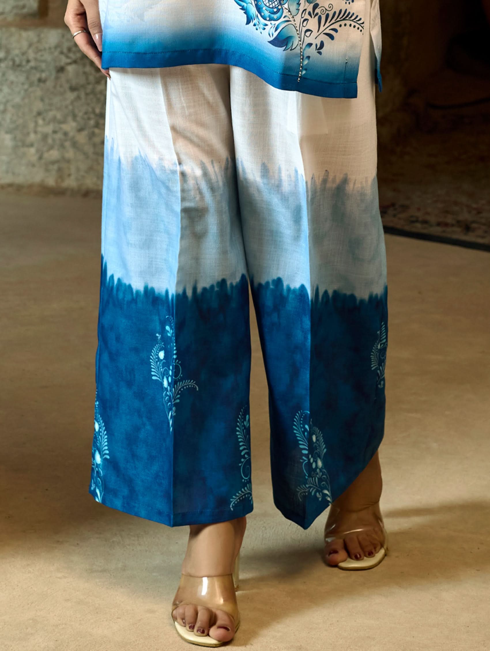 A woman wearing a digitally printed cotton linen short kurta with a revere collar and three-quarter sleeves, paired with straight pants. The outfit features blue and white colors with hand embroidery on the kurta.