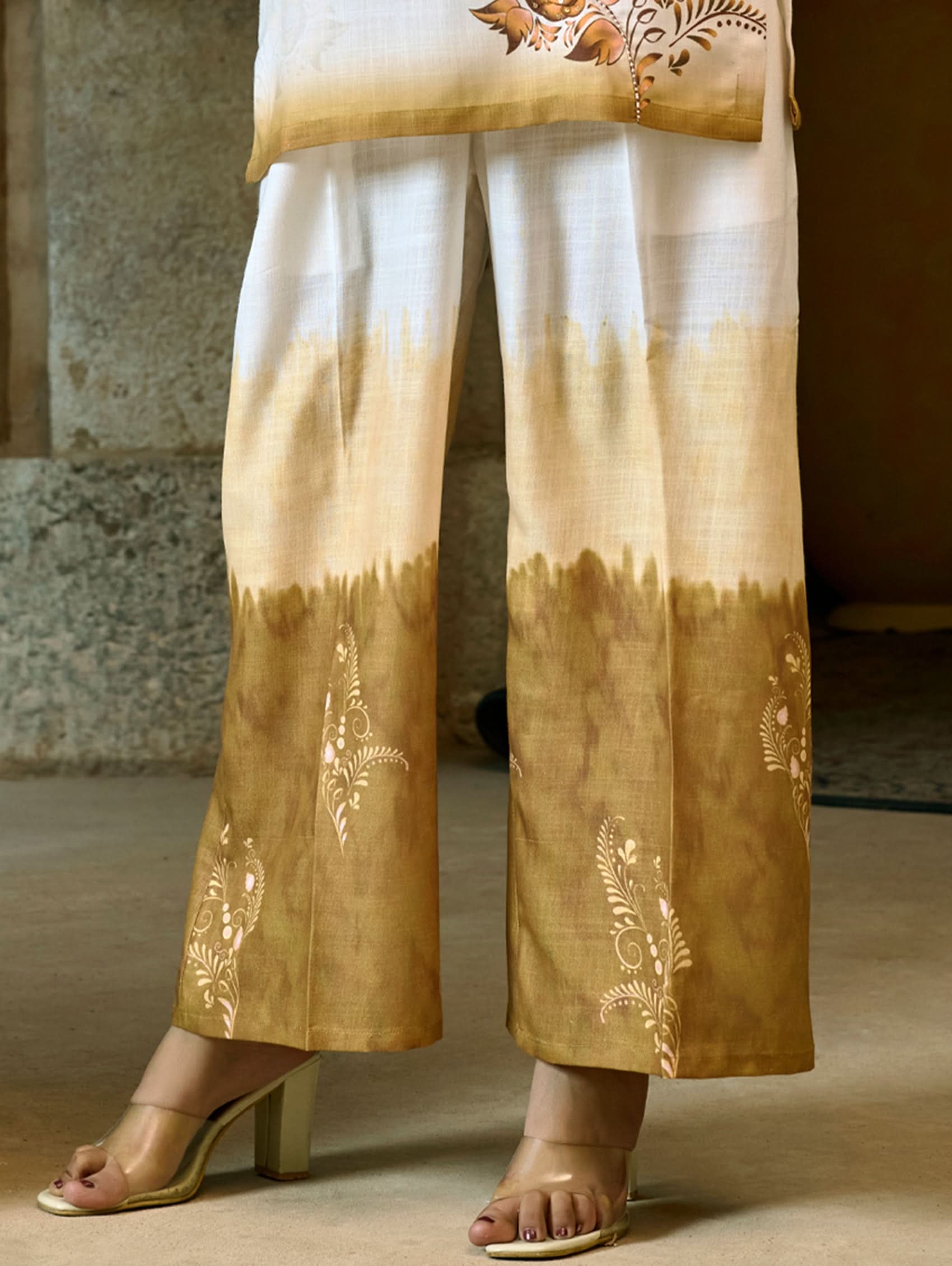 A woman wearing a digitally printed cotton linen short kurta with a revere collar and three-quarter sleeves, paired with straight pants. The outfit features white and golden colors with hand embroidery on the kurta.