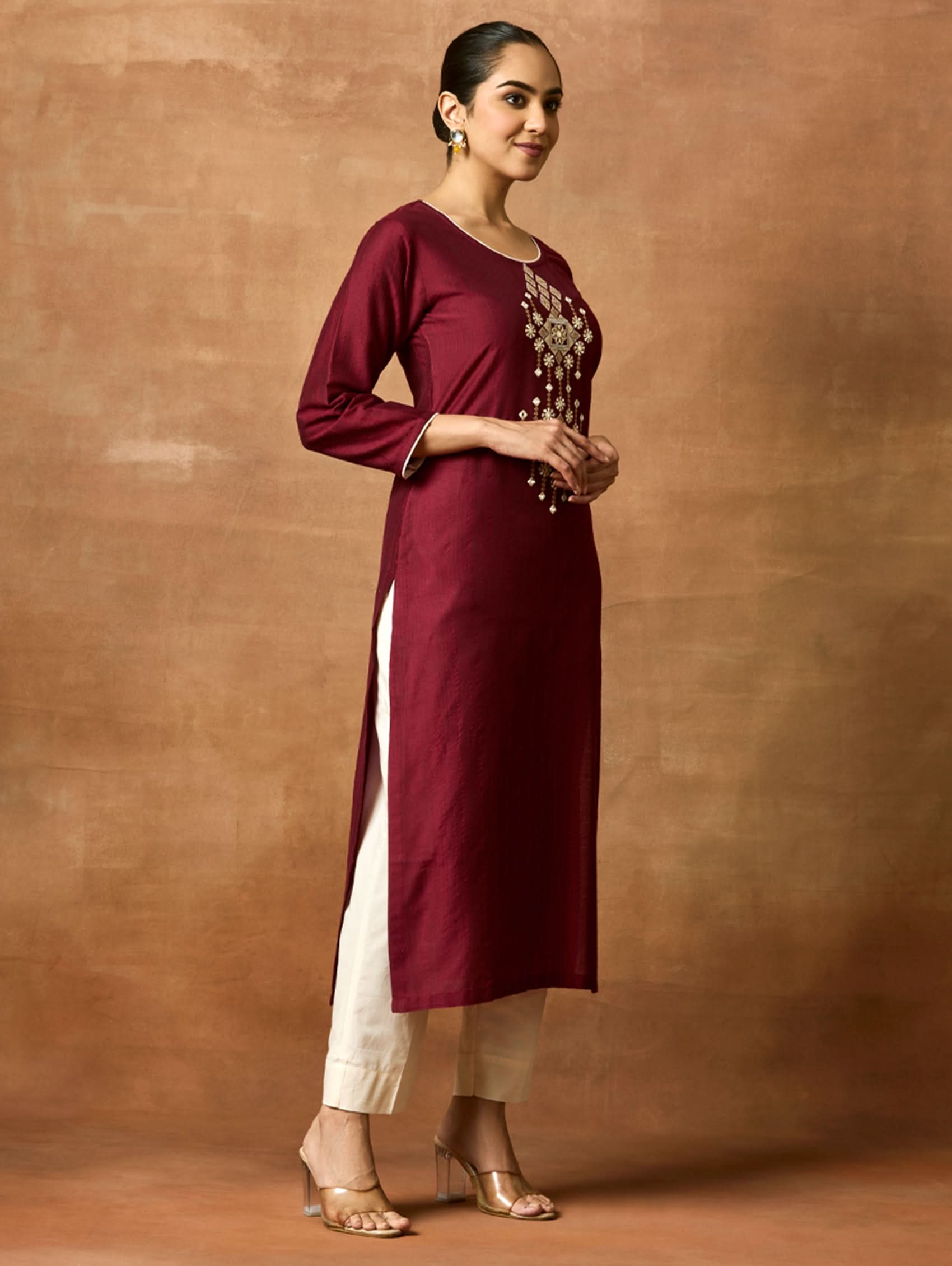Woman wearing a maroon and white kurta against a brown background