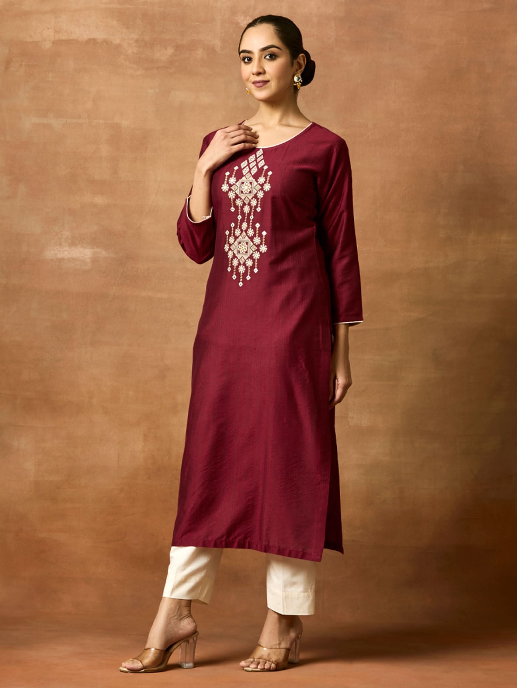 Woman wearing a maroon kurta with white pants against a brown background
