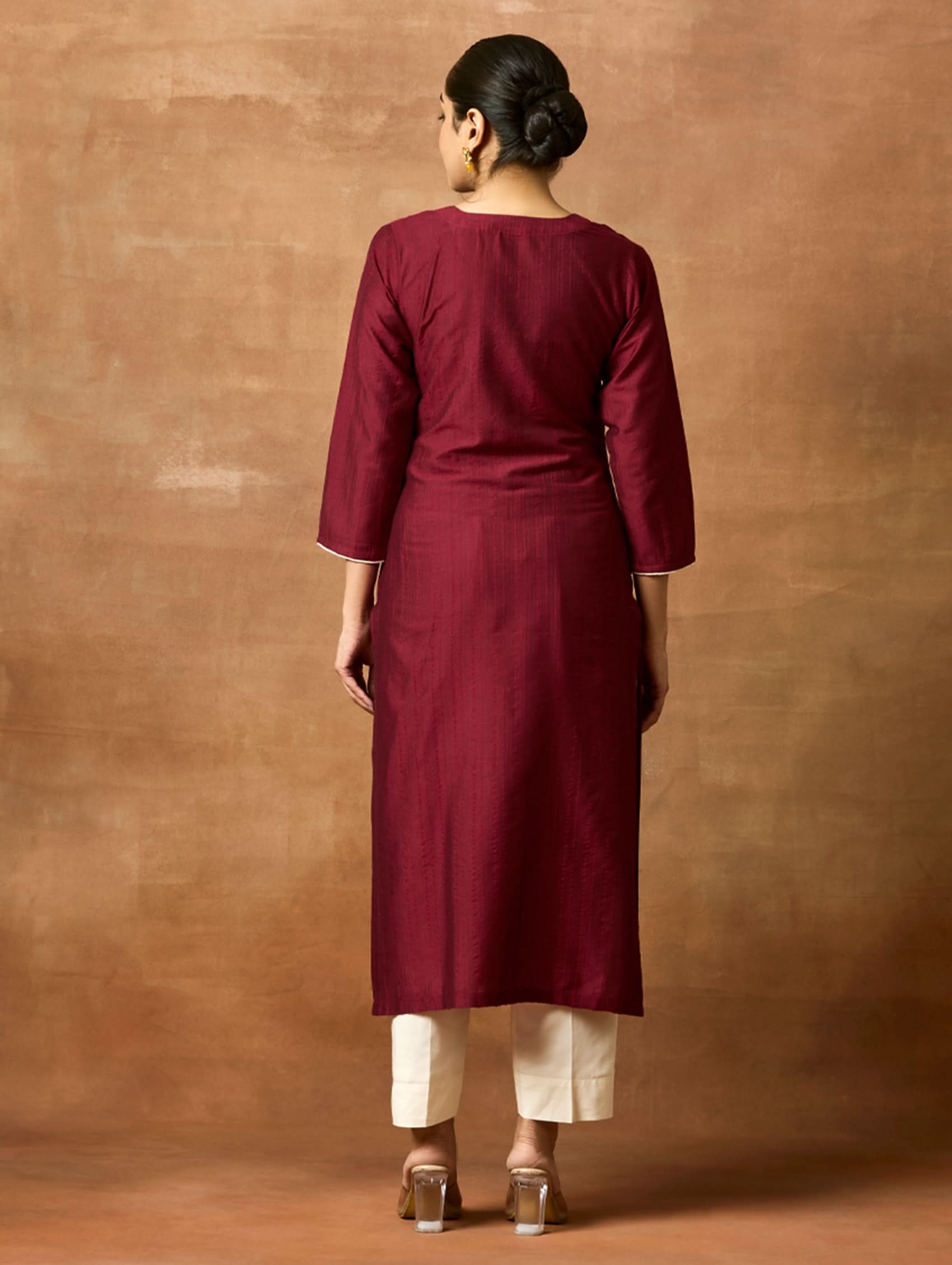 Person wearing a maroon kurta against a brown background