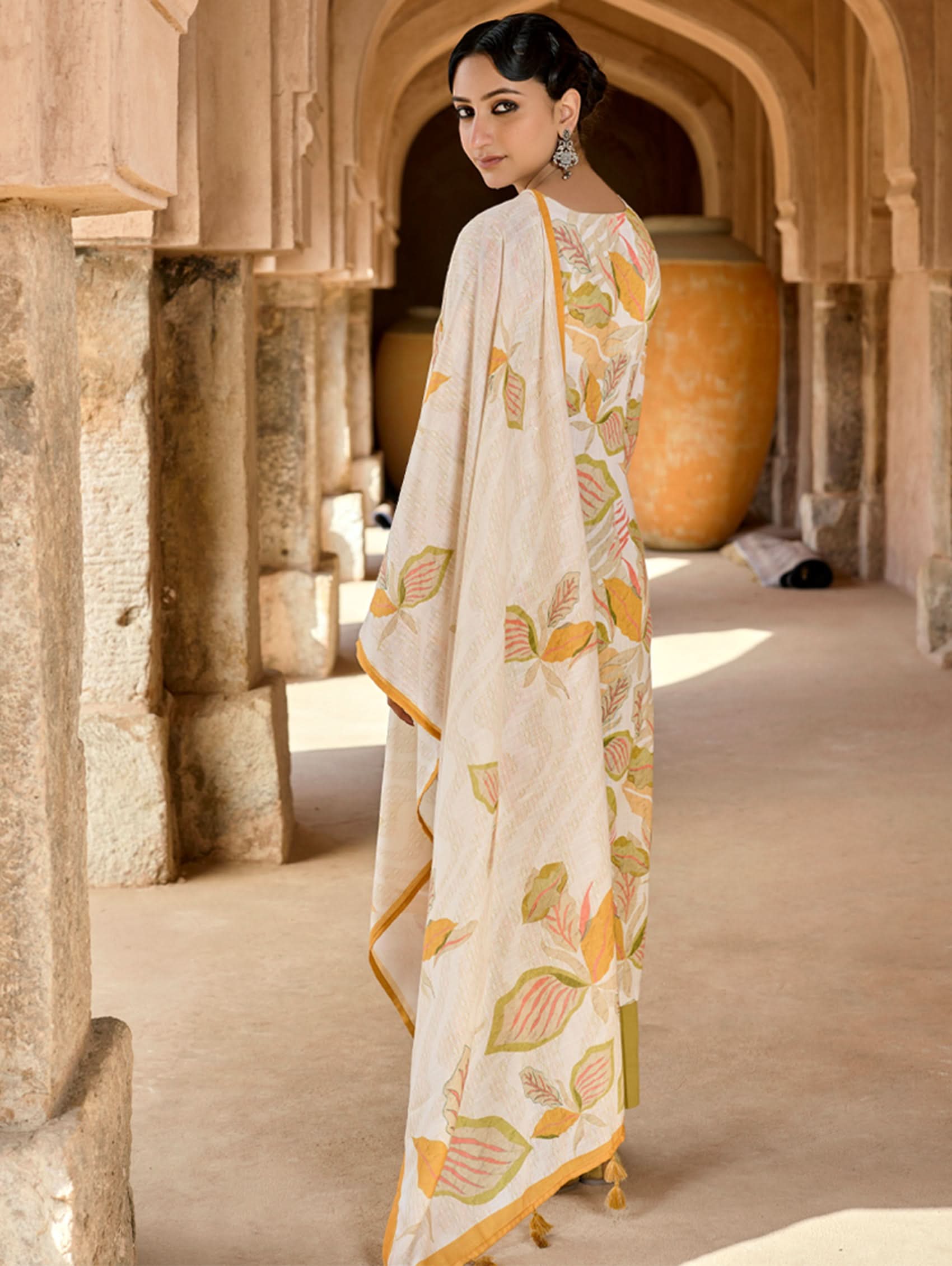 Woman in a patterned saree standing in a stone archway.