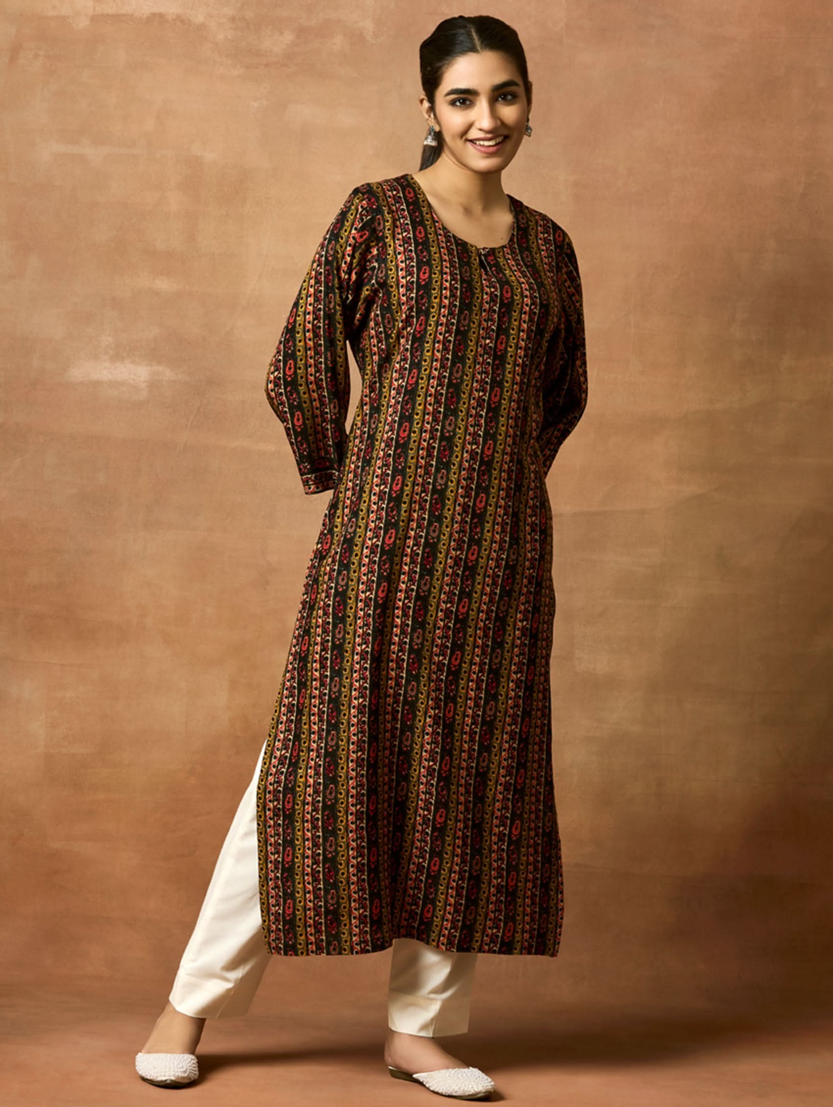 A woman plus-size model wearing a printed rayon kurta with keyhole round neckline and three-fourth sleeves. The kurta is in shades of brown and black with side slits.