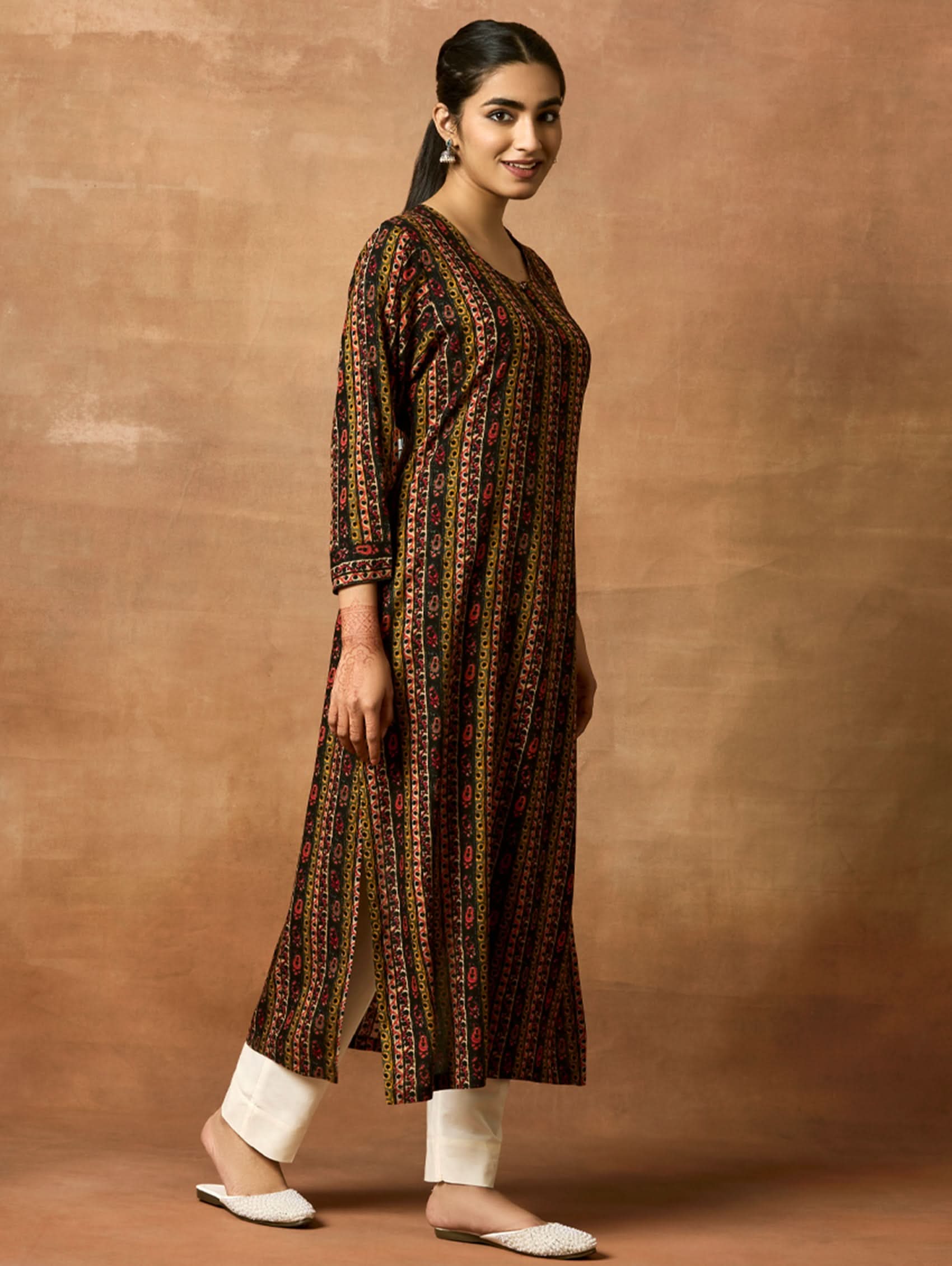 A woman plus-size model wearing a printed rayon kurta with keyhole round neckline and three-fourth sleeves. The kurta is in shades of brown and black with side slits.