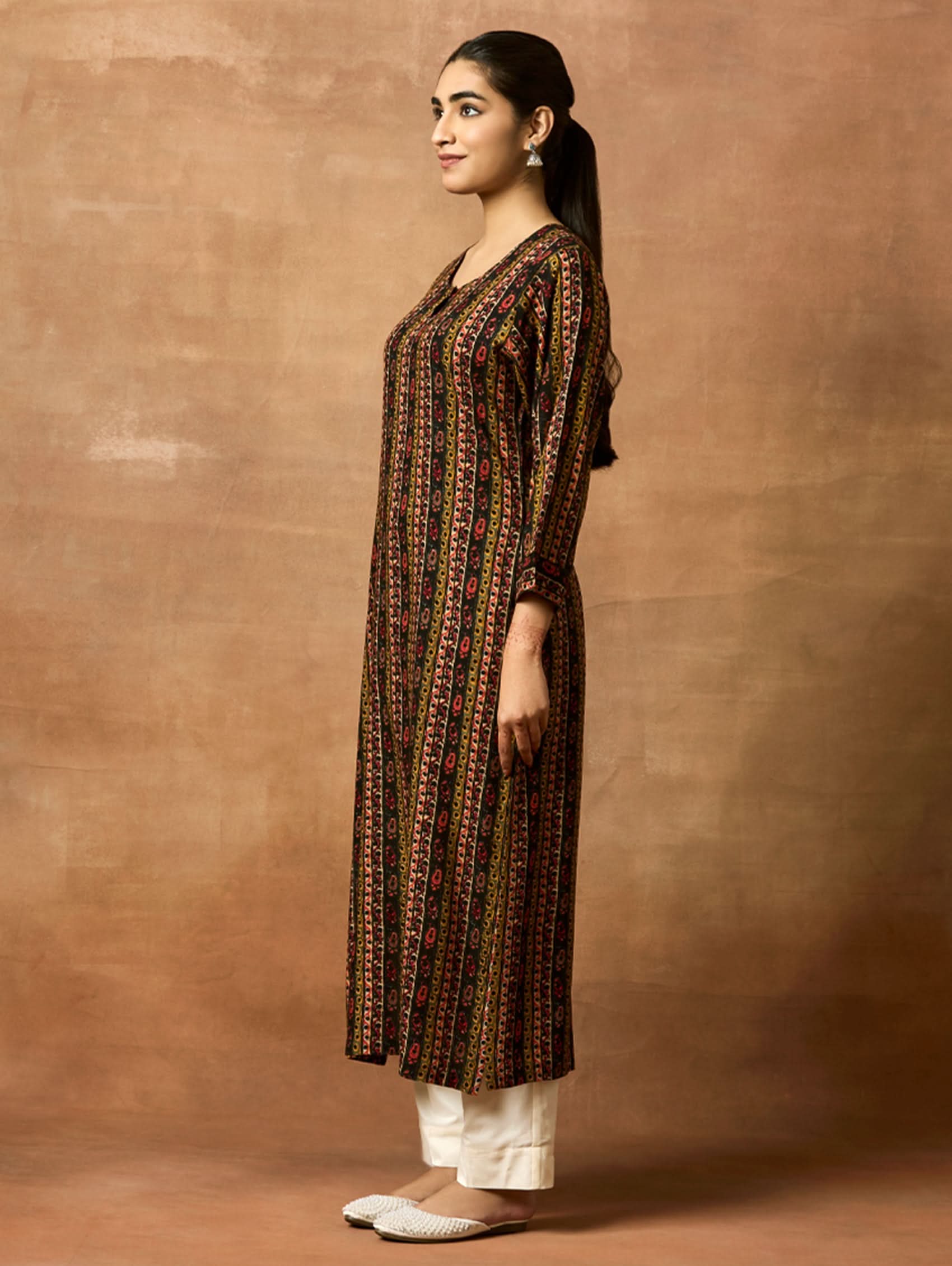 A woman plus-size model wearing a printed rayon kurta with keyhole round neckline and three-fourth sleeves. The kurta is in shades of brown and black with side slits.