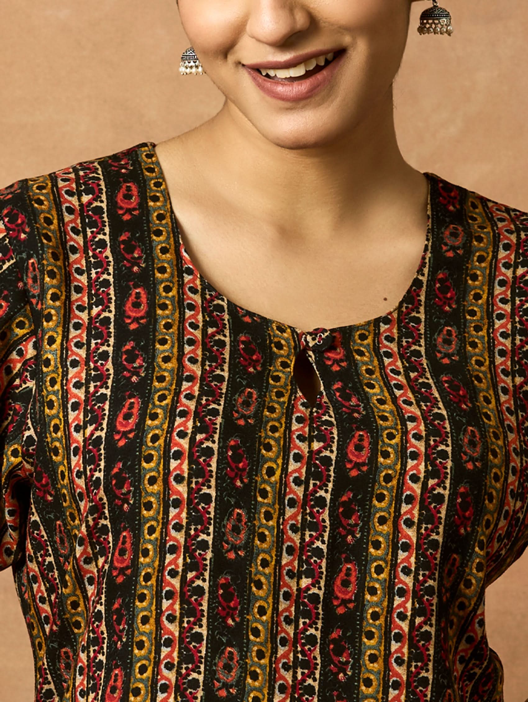 A woman plus-size model wearing a printed rayon kurta with keyhole round neckline and three-fourth sleeves. The kurta is in shades of brown and black with side slits.