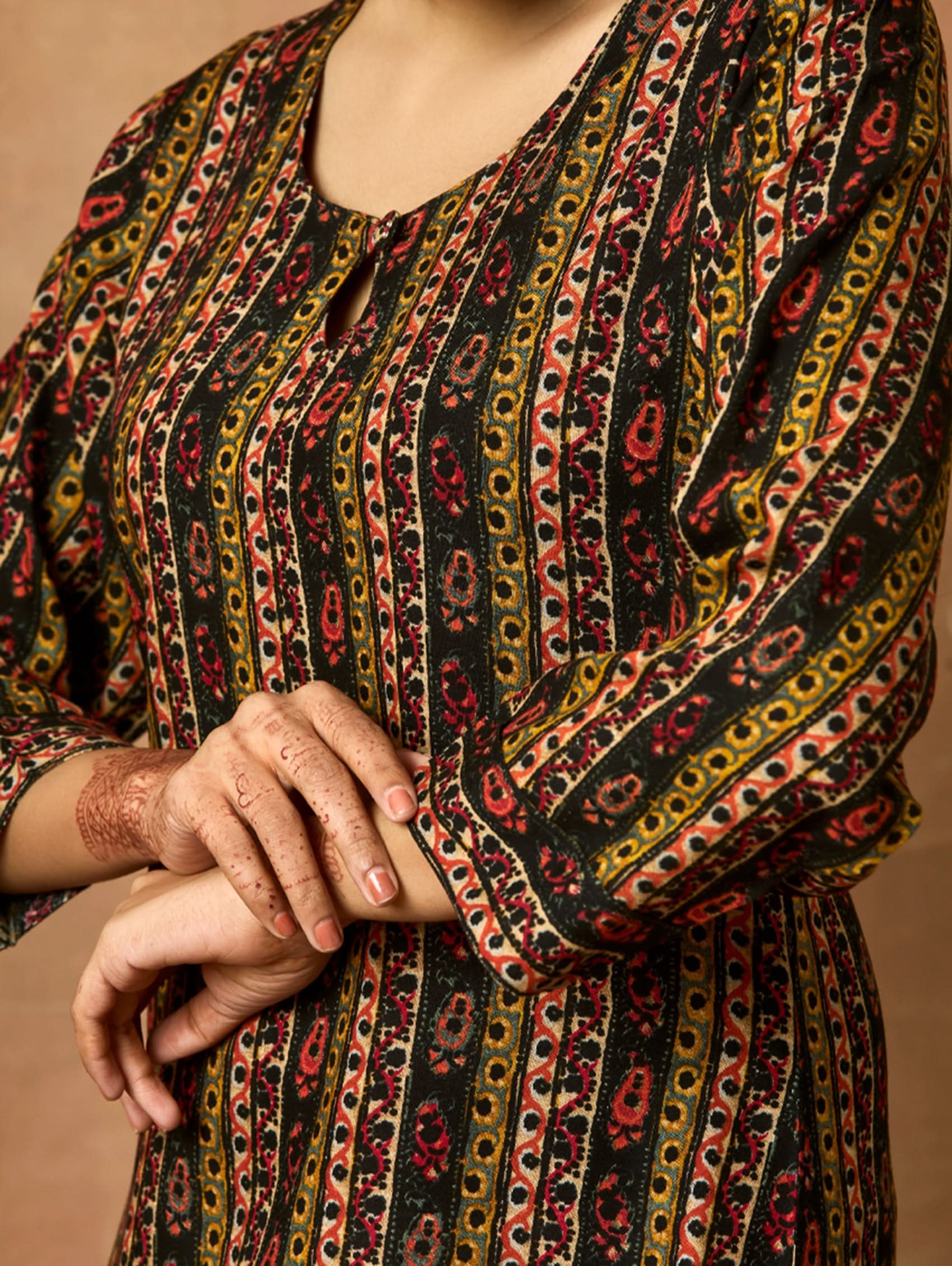 A woman plus-size model wearing a printed rayon kurta with keyhole round neckline and three-fourth sleeves. The kurta is in shades of brown and black with side slits.