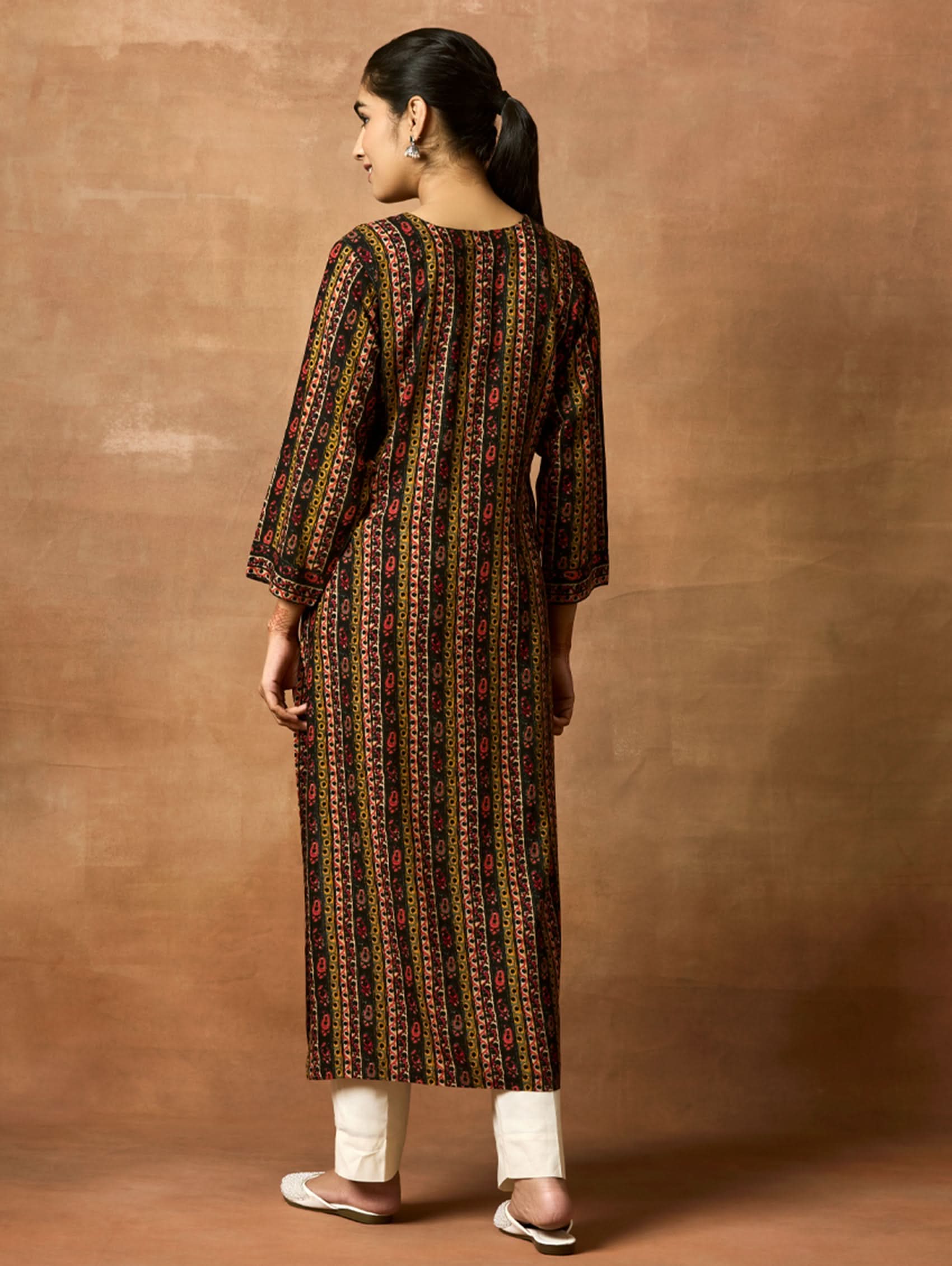A woman plus-size model wearing a printed rayon kurta with keyhole round neckline and three-fourth sleeves. The kurta is in shades of brown and black with side slits.