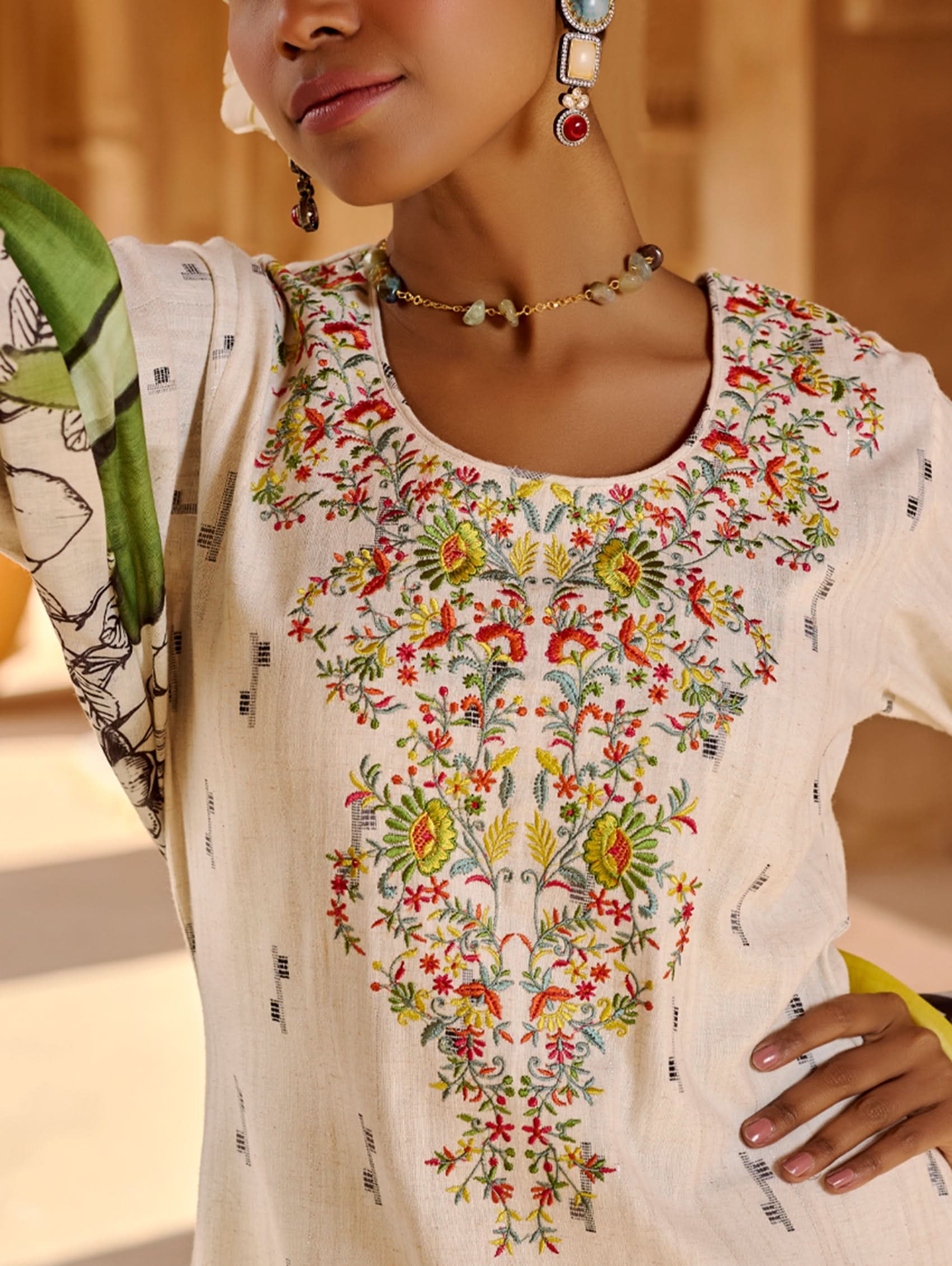 A woman modeling a white kurta with three-fourth sleeves, round neckline, and side slits, paired with straight pants and a multicolored dupatta with geometric patterns.