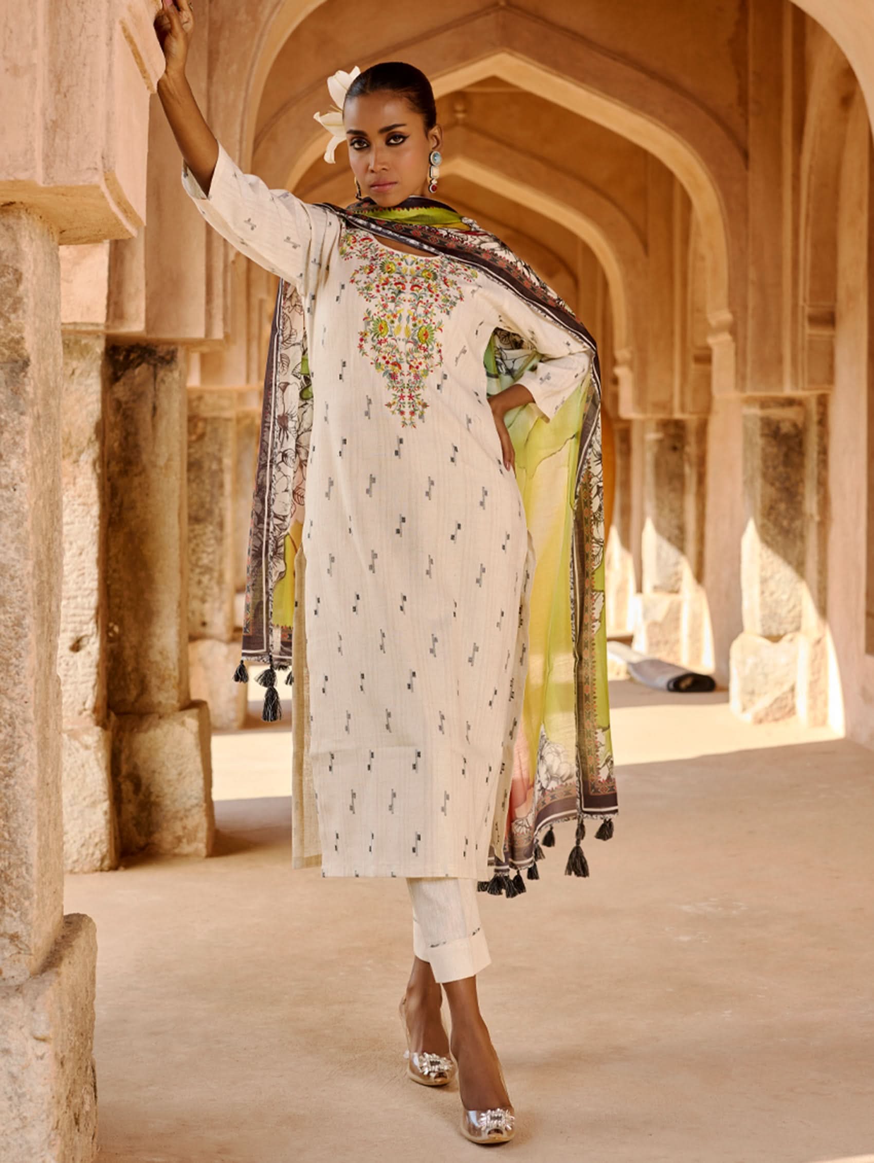A woman modeling a white kurta with three-fourth sleeves, round neckline, and side slits, paired with straight pants and a multicolored dupatta with geometric patterns.