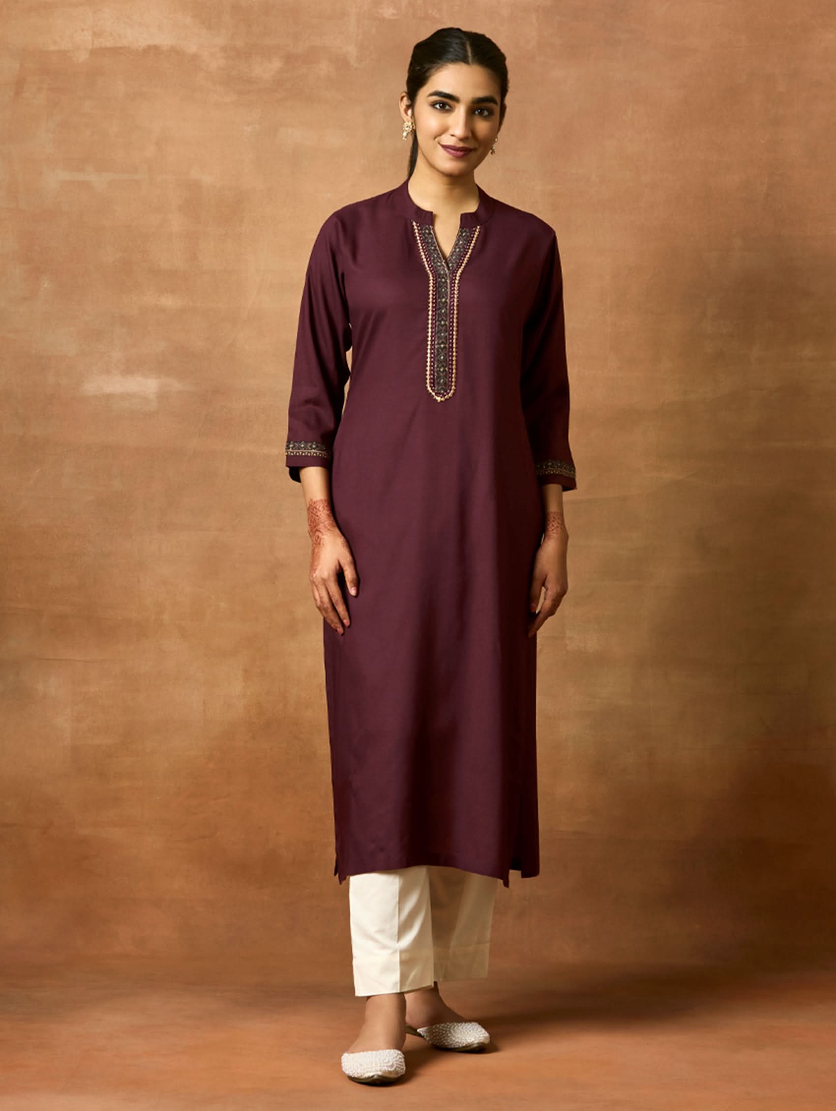 A woman plus size model wearing a maroon viscose rayon kurta with a ban collar, three-fourth sleeves, and side slits, with computerised thread embroidery on the kurta.