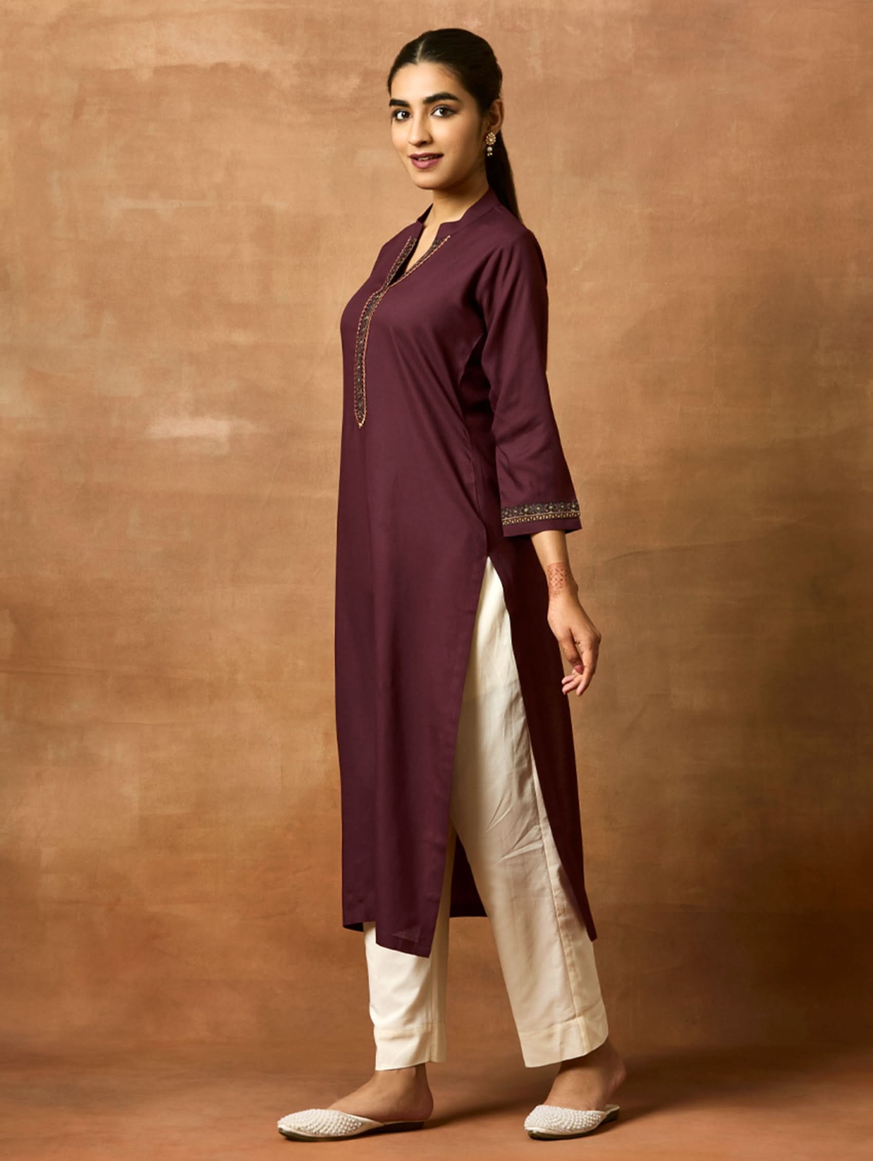 A woman plus size model wearing a maroon viscose rayon kurta with a ban collar, three-fourth sleeves, and side slits, with computerised thread embroidery on the kurta.