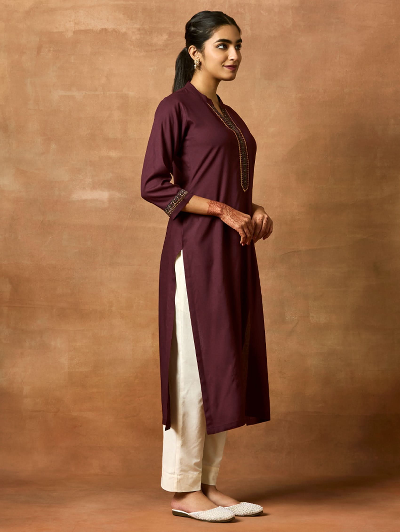A woman plus size model wearing a maroon viscose rayon kurta with a ban collar, three-fourth sleeves, and side slits, with computerised thread embroidery on the kurta.