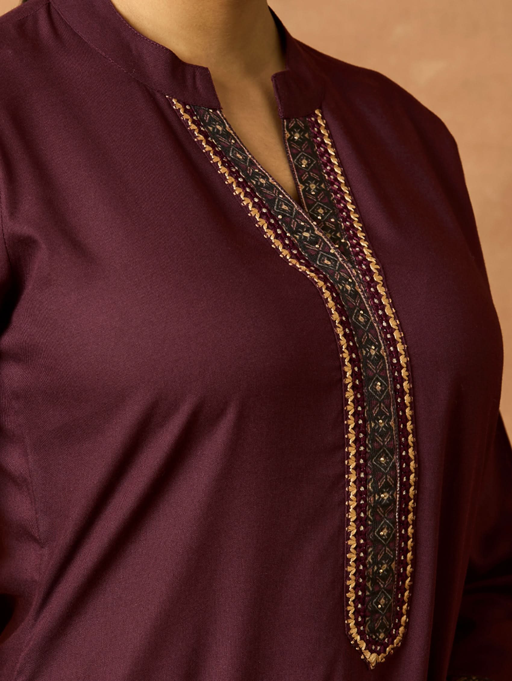 A woman plus size model wearing a maroon viscose rayon kurta with a ban collar, three-fourth sleeves, and side slits, with computerised thread embroidery on the kurta.