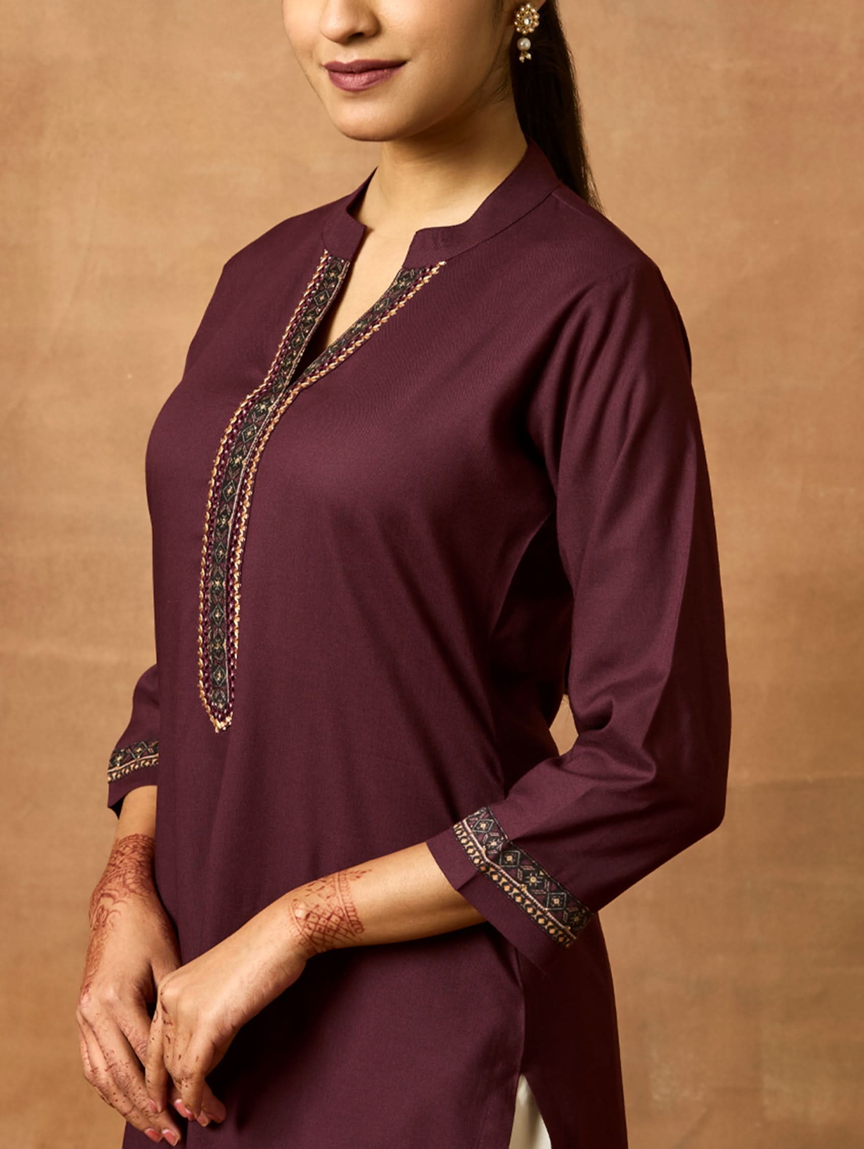 A woman plus size model wearing a maroon viscose rayon kurta with a ban collar, three-fourth sleeves, and side slits, with computerised thread embroidery on the kurta.