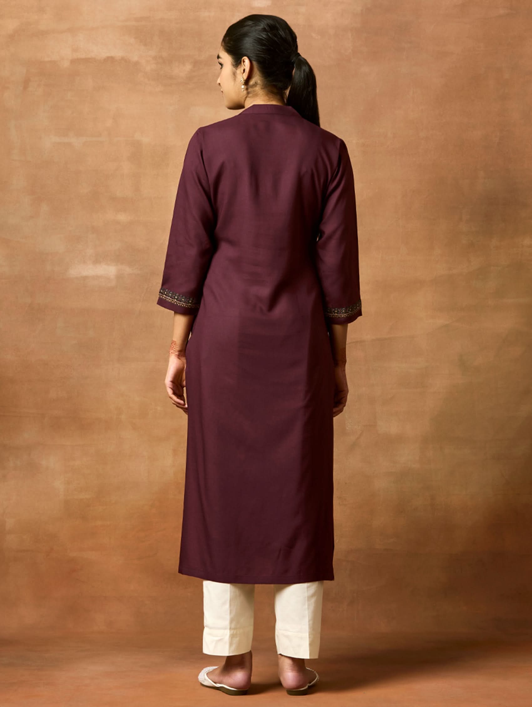 A woman plus size model wearing a maroon viscose rayon kurta with a ban collar, three-fourth sleeves, and side slits, with computerised thread embroidery on the kurta.