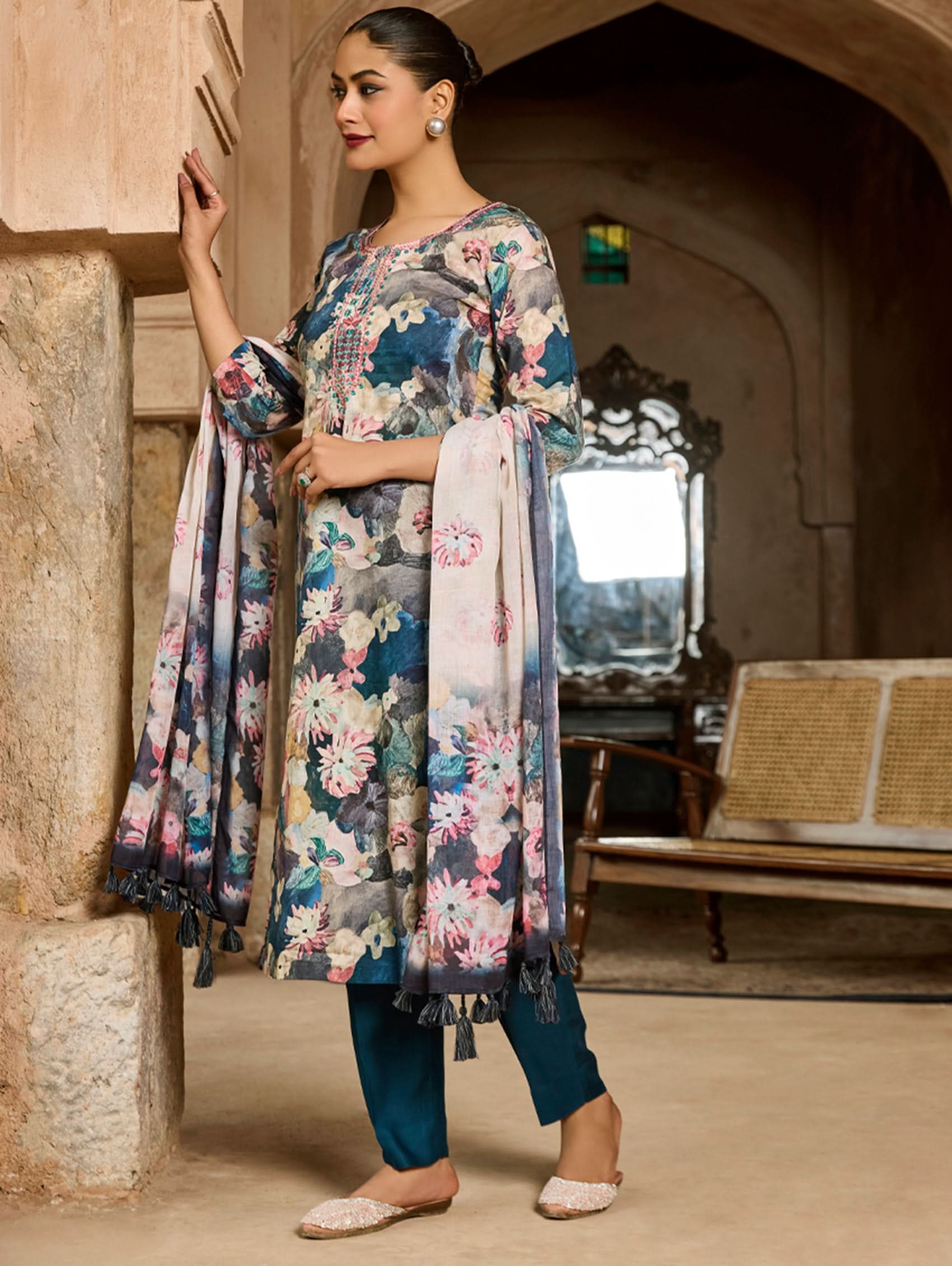 A woman wearing a floral malai cotton suit set with embroidered details,and printed consisting of a kurta, pants, and a printed weave silk dupatta.