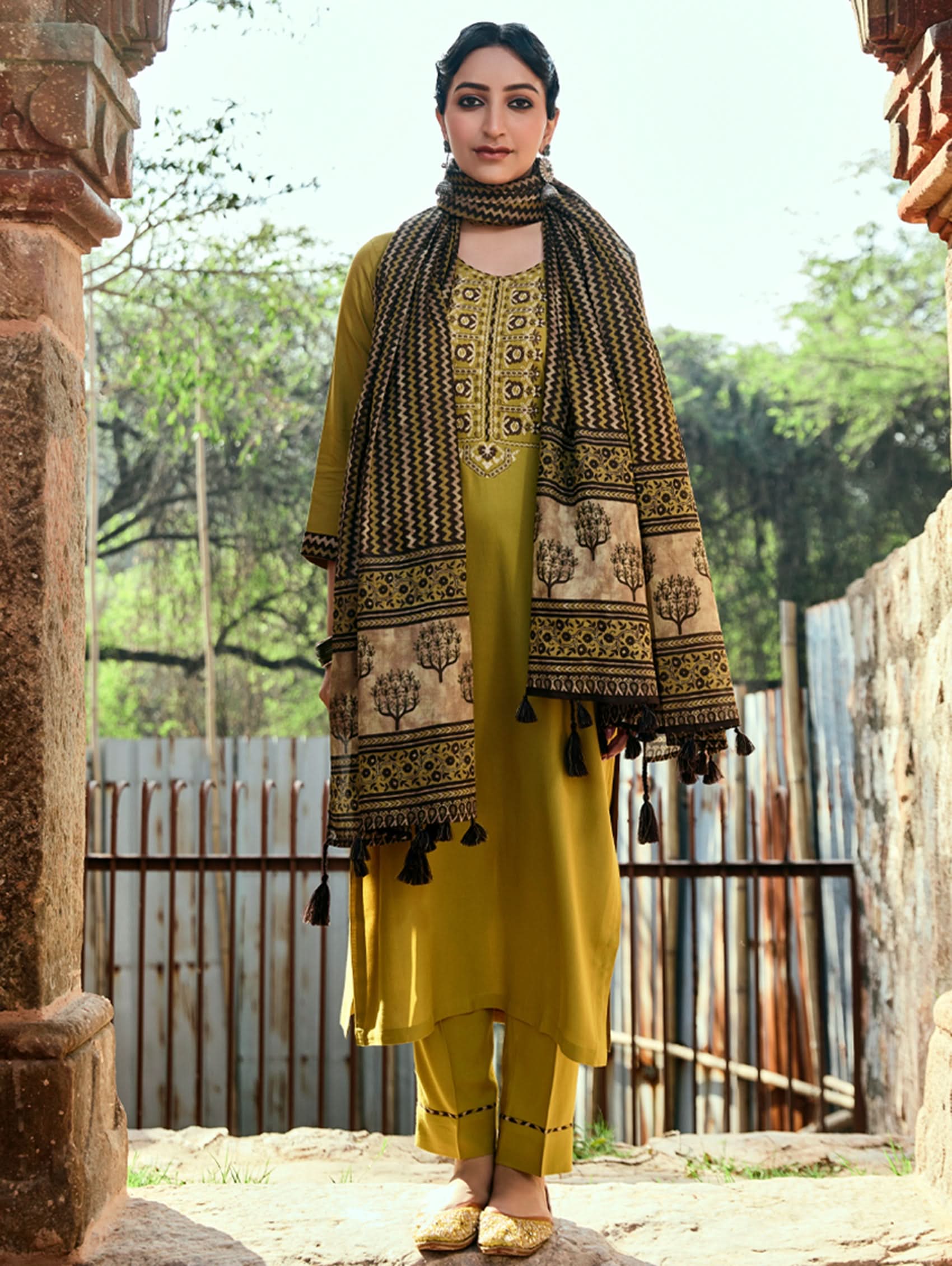 A woman wearing a yellow viscose rayon suit set with embroidery, including a kurta with three-fourth sleeves and a round neckline, pants with pockets, and a printed dupatta.