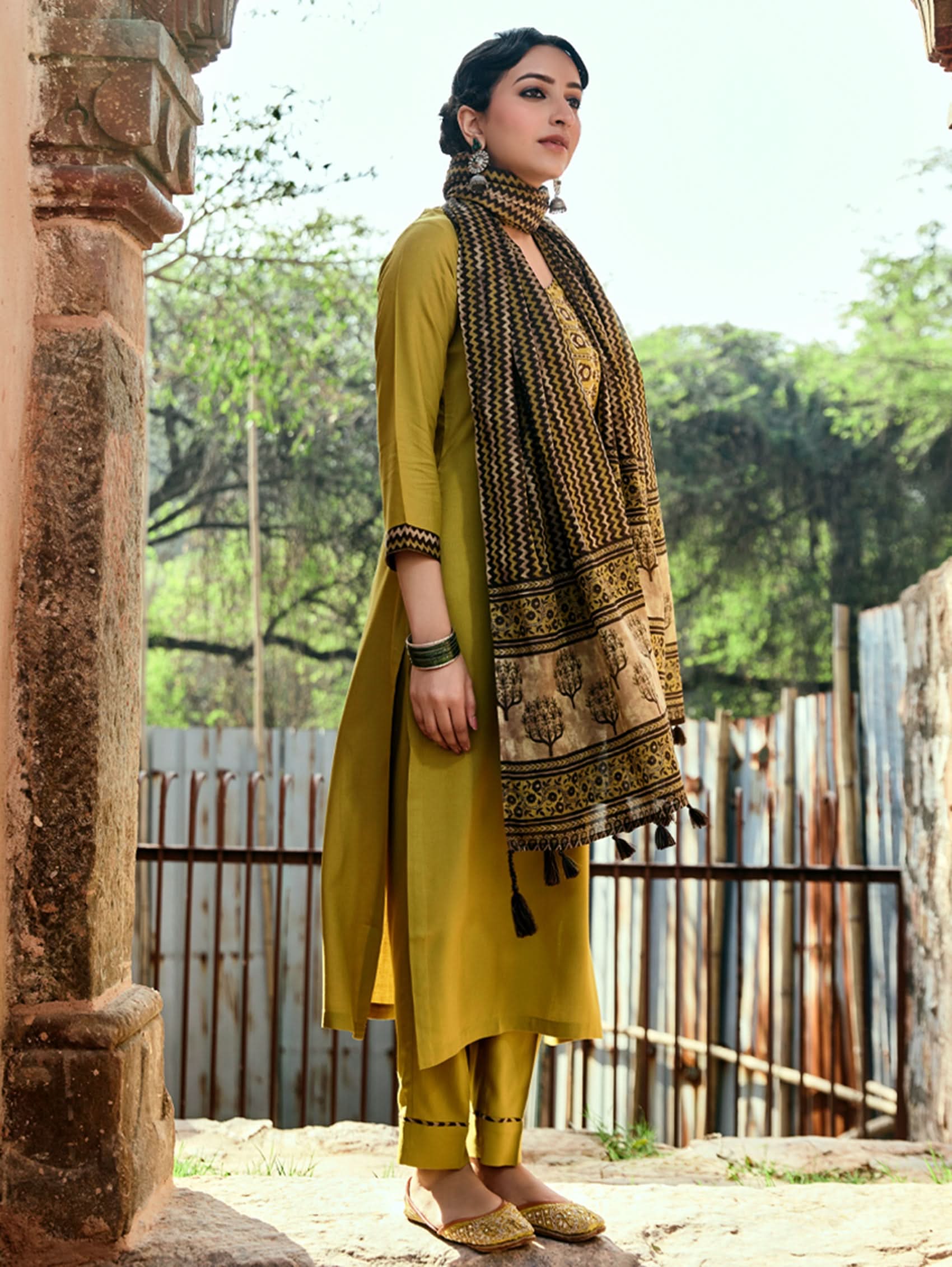 A woman wearing a yellow viscose rayon suit set with embroidery, including a kurta with three-fourth sleeves and a round neckline, pants with pockets, and a printed dupatta.