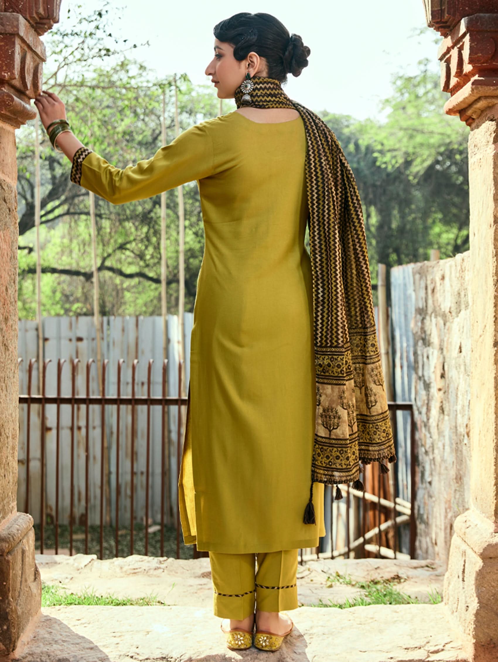A woman wearing a yellow viscose rayon suit set with embroidery, including a kurta with three-fourth sleeves and a round neckline, pants with pockets, and a printed dupatta.