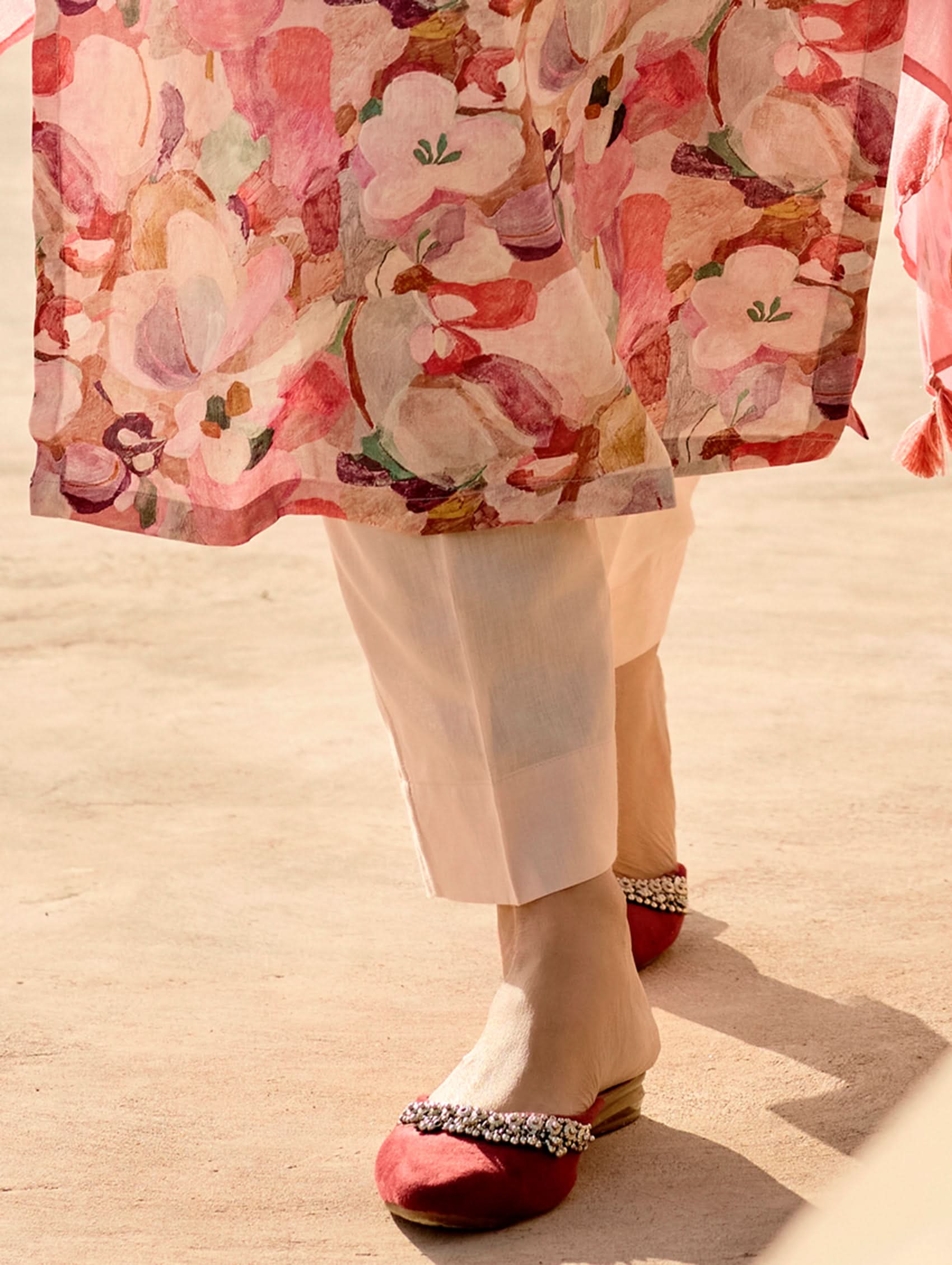 A woman standing in an archway, wearing a digitally printed cotton linen suit set with a round neckline kurta, three-fourth sleeves, side slits, and a dupatta with a floral pattern.
