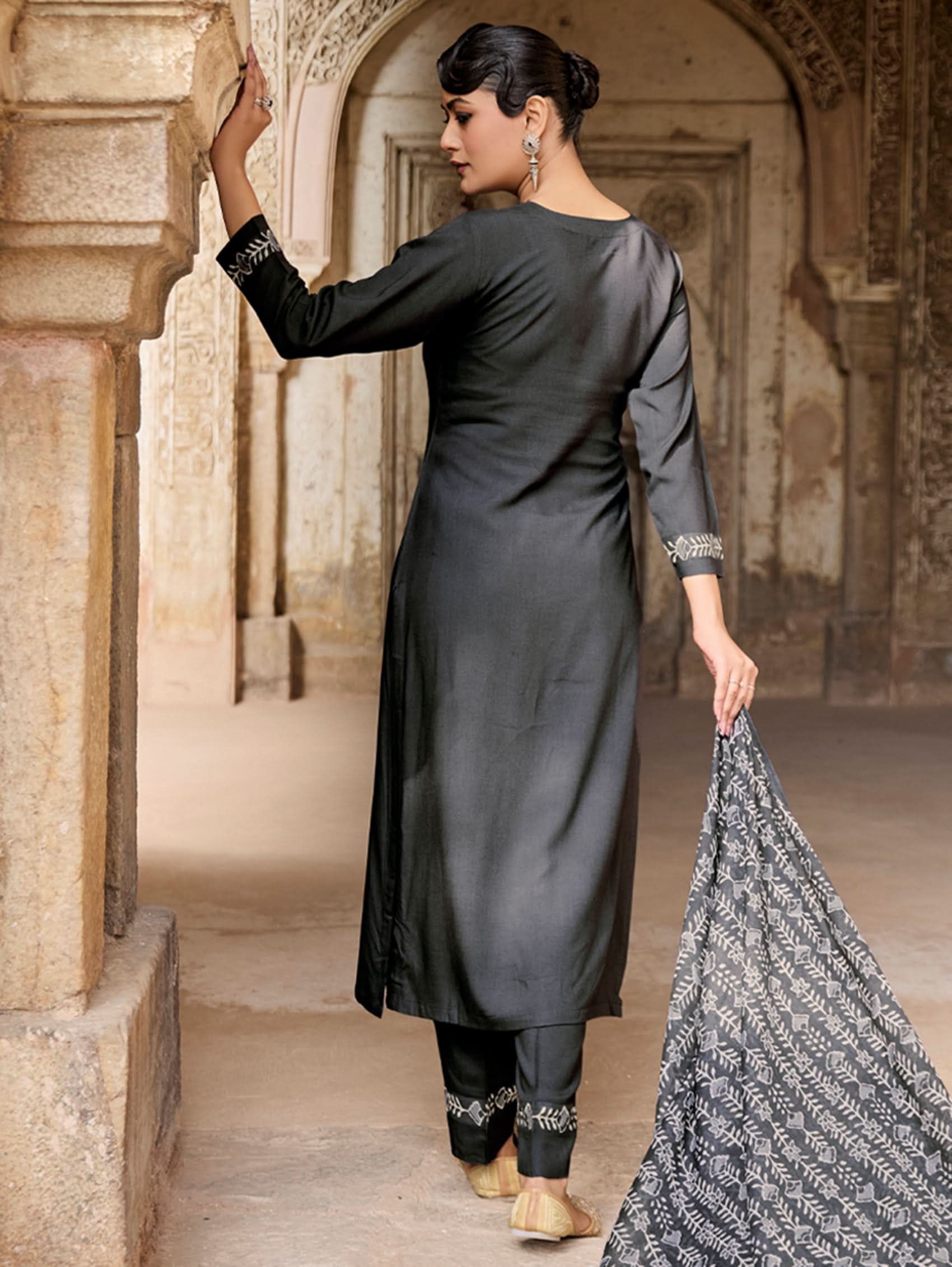 Woman in black traditional outfit holding a patterned fabric in an architectural setting.