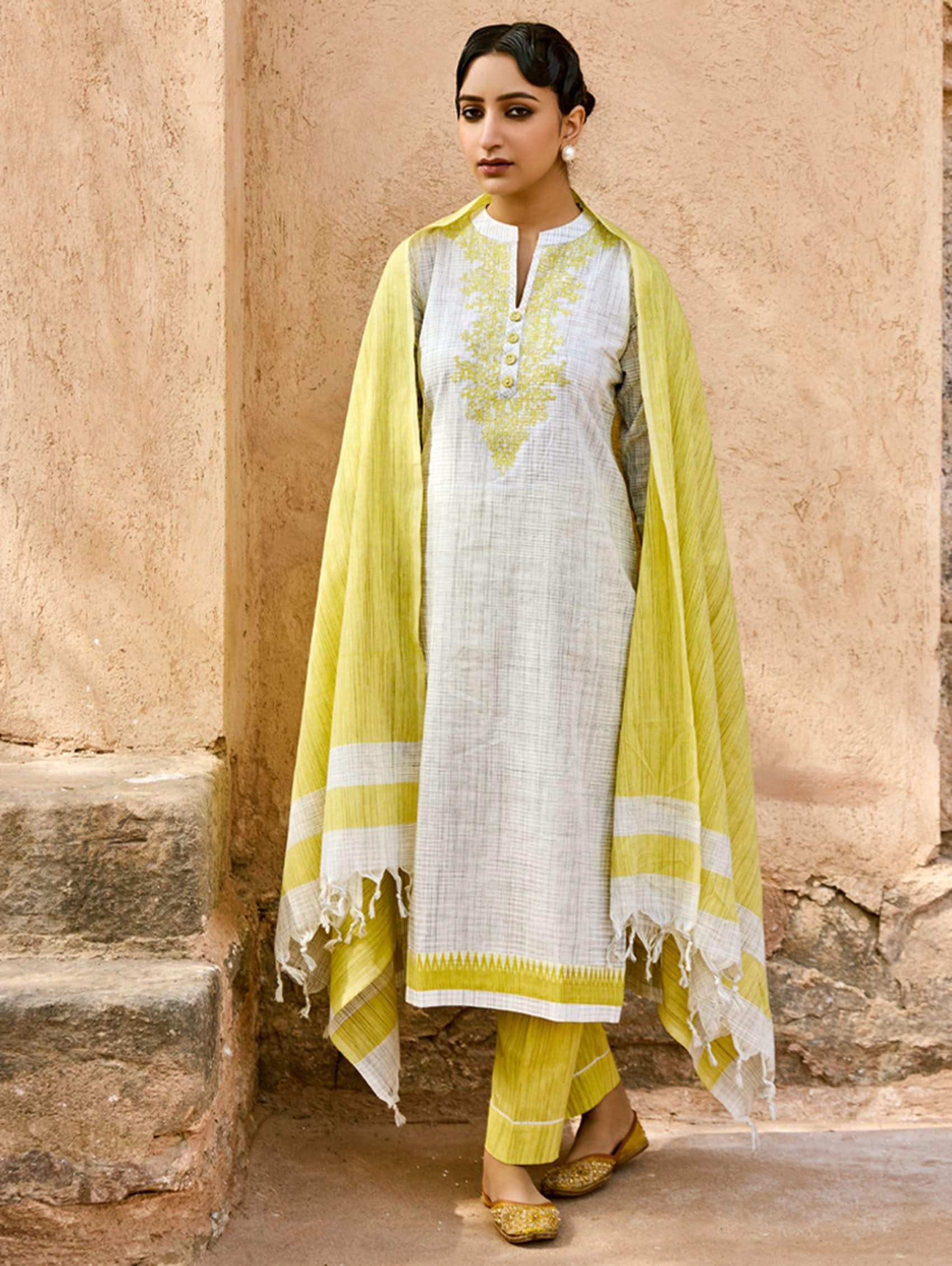 A woman wearing a traditional cotton suit set with embroidery, consisting of a kurta, pants, and a dupatta, in white, green, and beige colors.