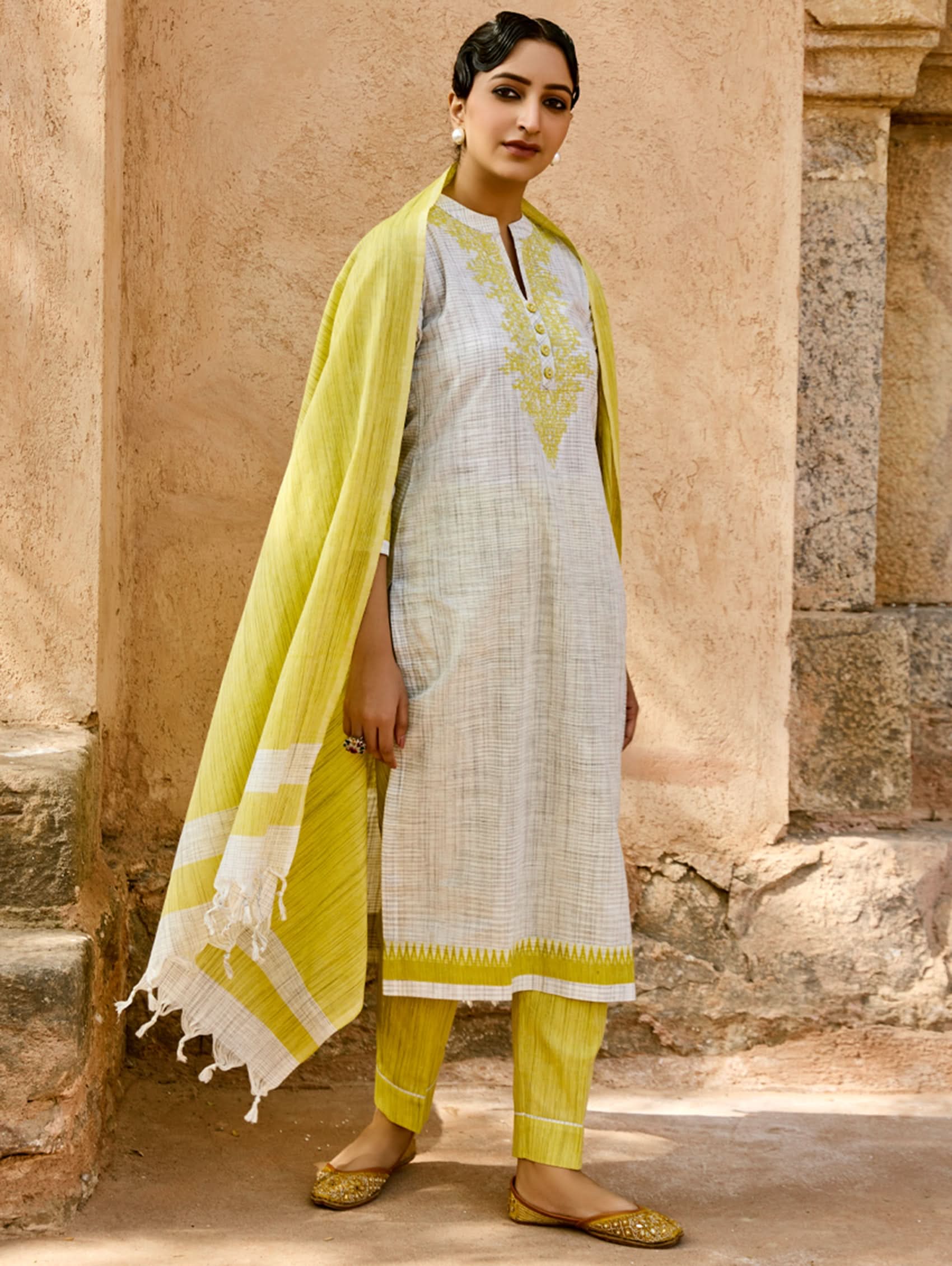 Woman wearing a traditional outfit with a yellow dupatta in front of stone architecture
