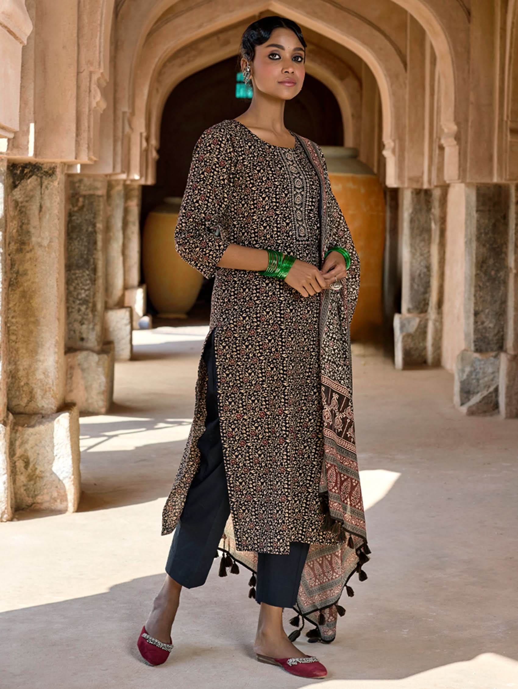 A woman standing in a doorway wearing a traditional Ajrakh print pure cotton suit set with a kurta, pants, and a dupatta.