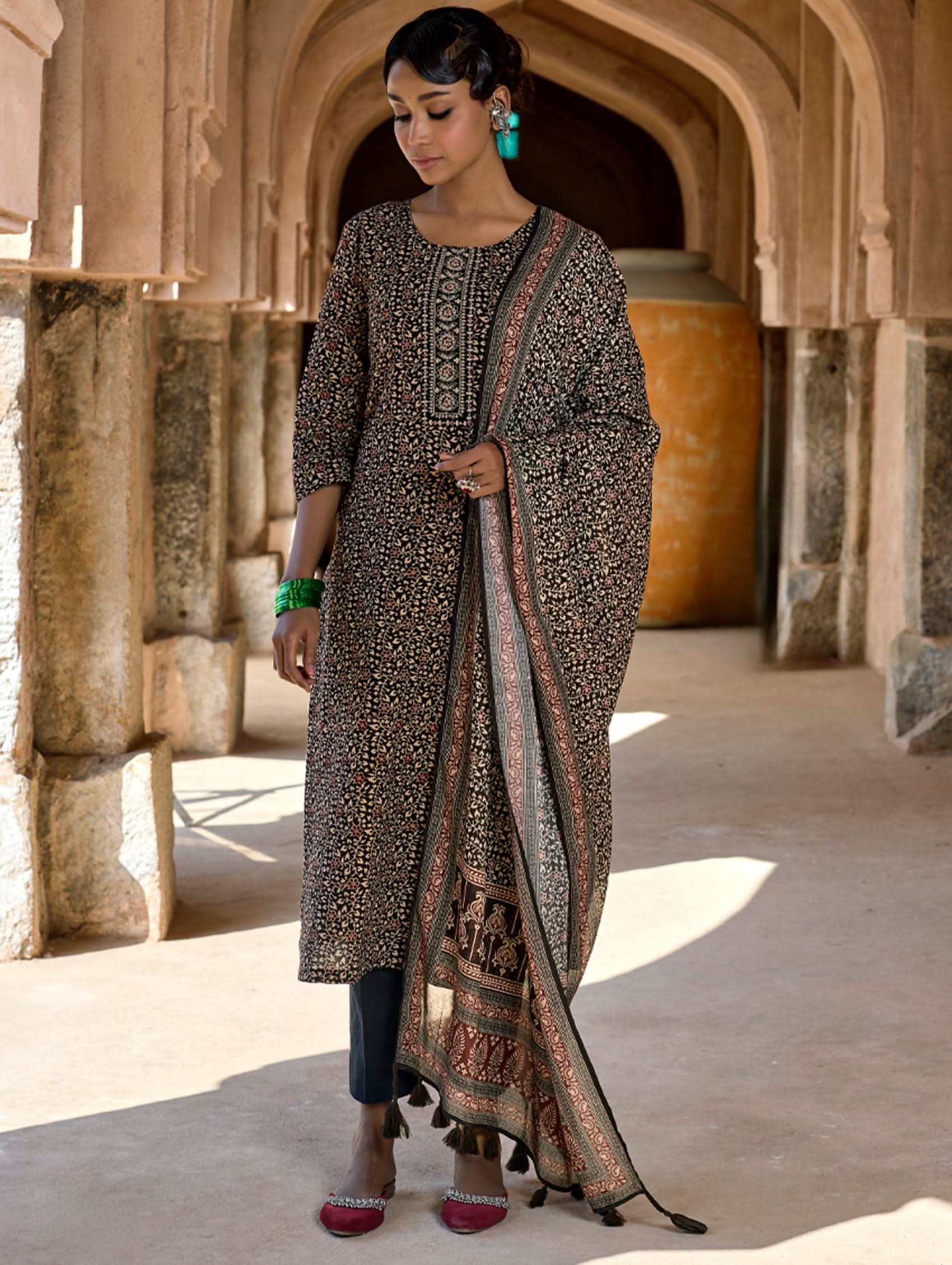 Woman in traditional outfit with patterned dress and dupatta in an archway.