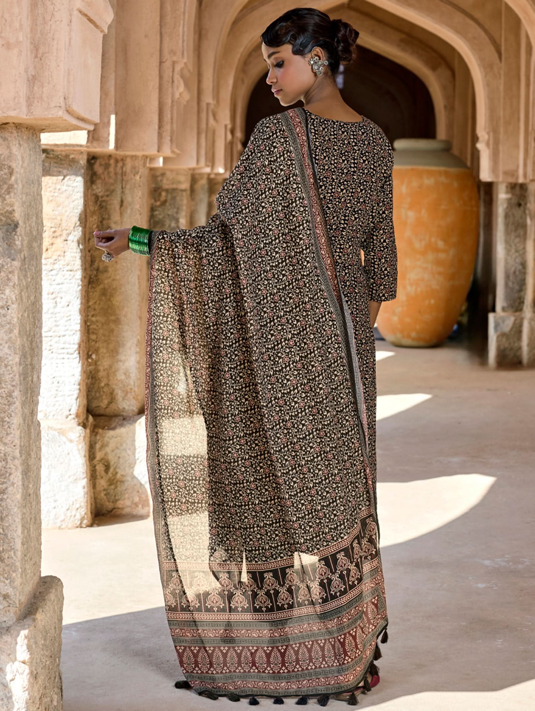 Woman in a patterned saree standing in a architectural setting