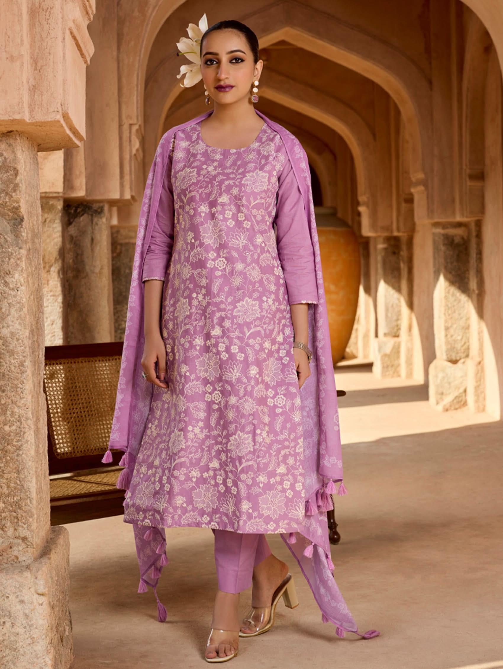 A woman standing in a hallway wearing a purple floral embroidered pure cotton suit set with a kurta, pants, and a dupatta.