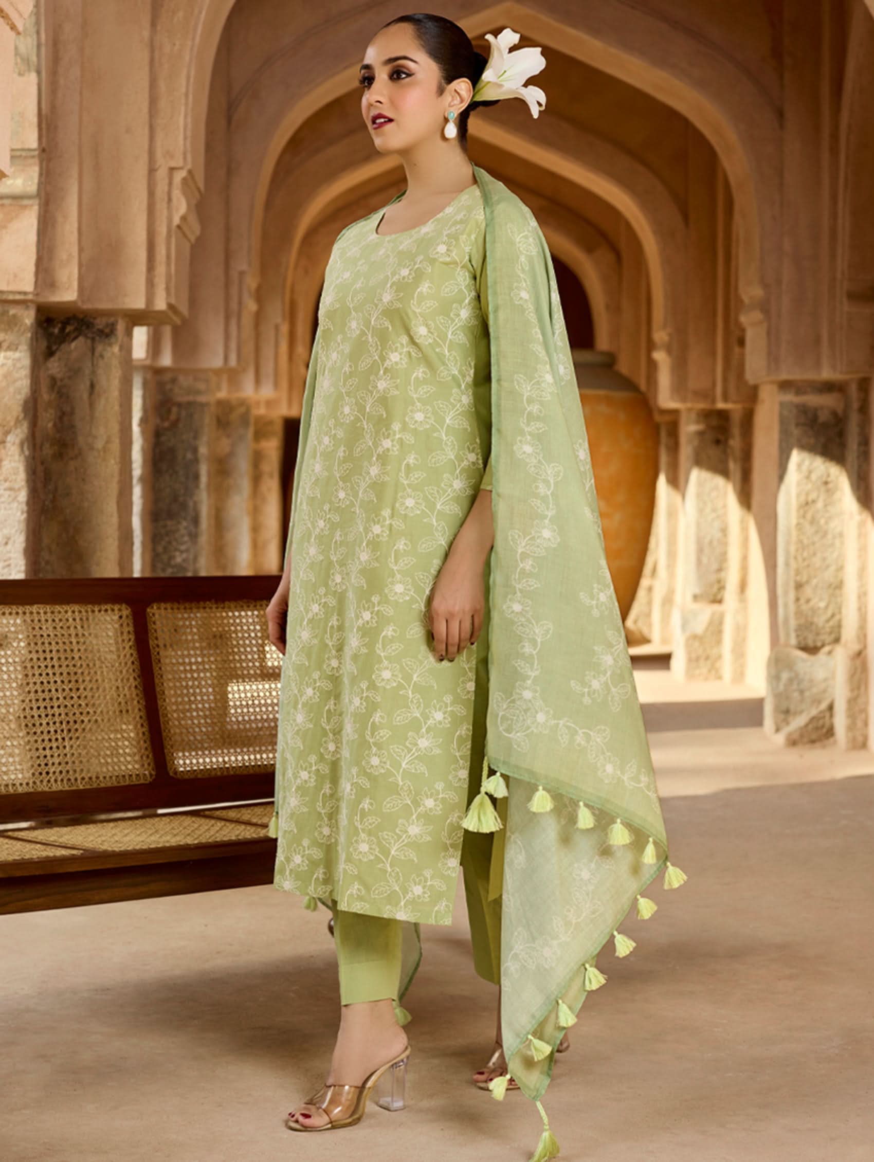 Woman in a light green traditional outfit with a dupatta in a decorative setting.